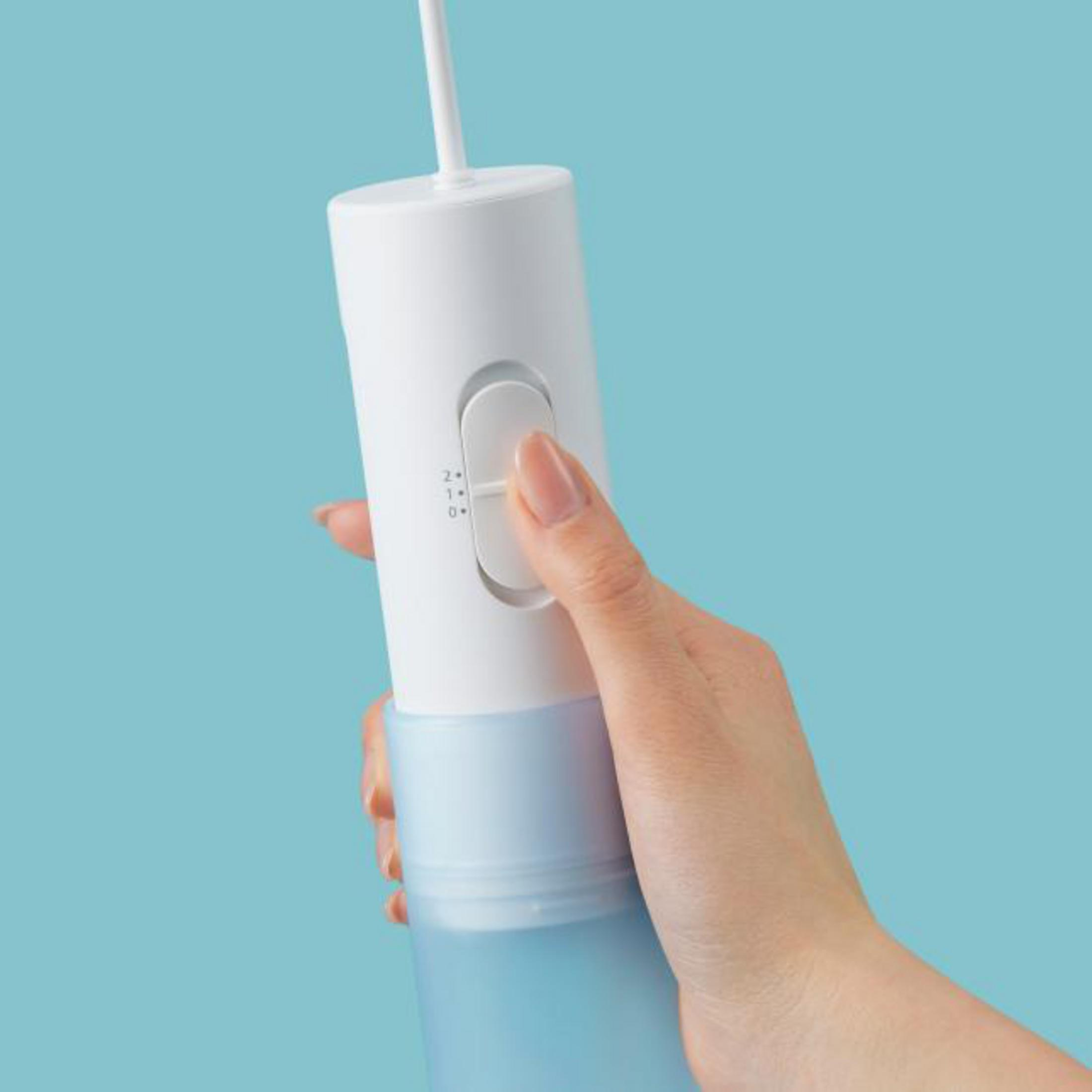Una mano tiene un idropulsore bianco e blu su sfondo blu chiaro.