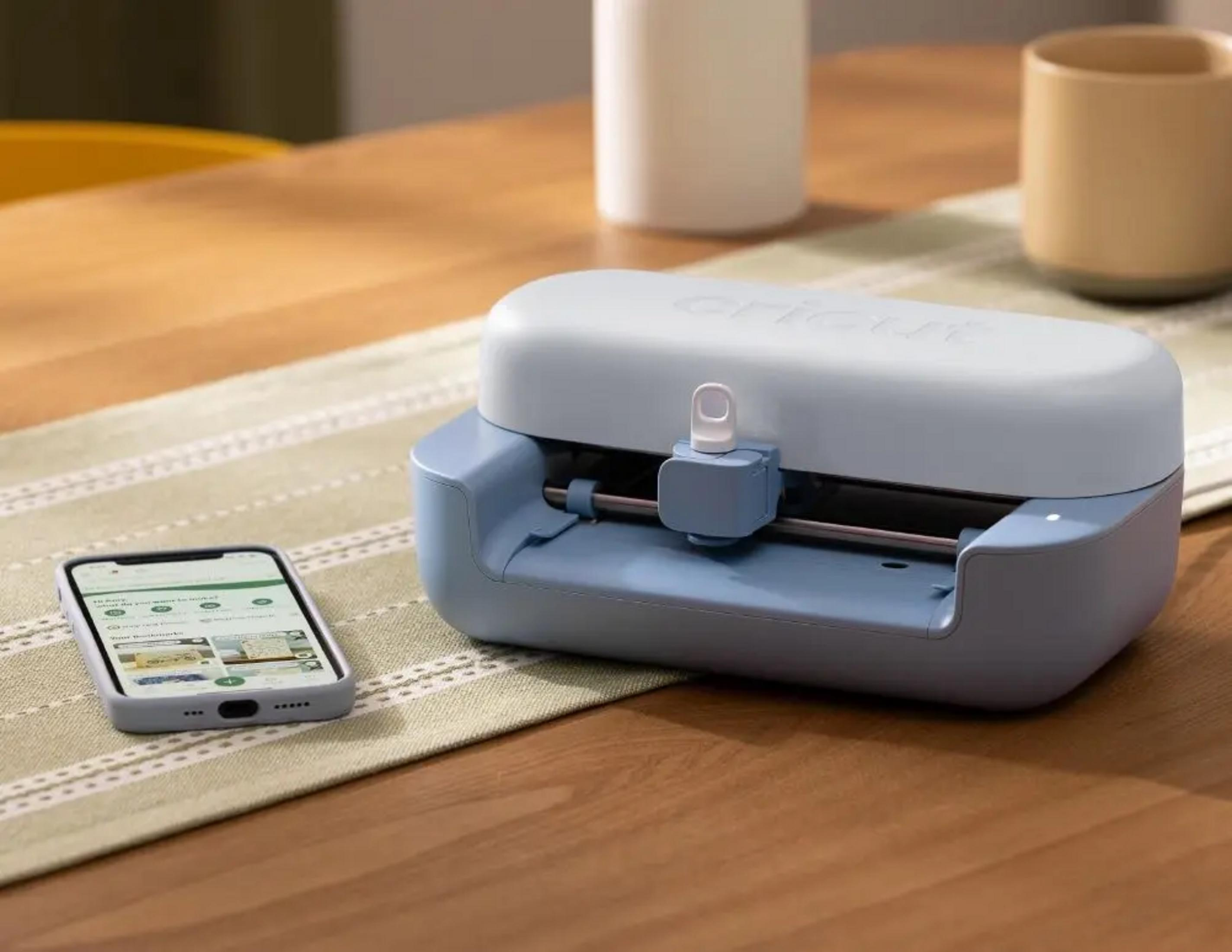 Una máquina de corte azul y gris claro con un smartphone al lado sobre una mesa.