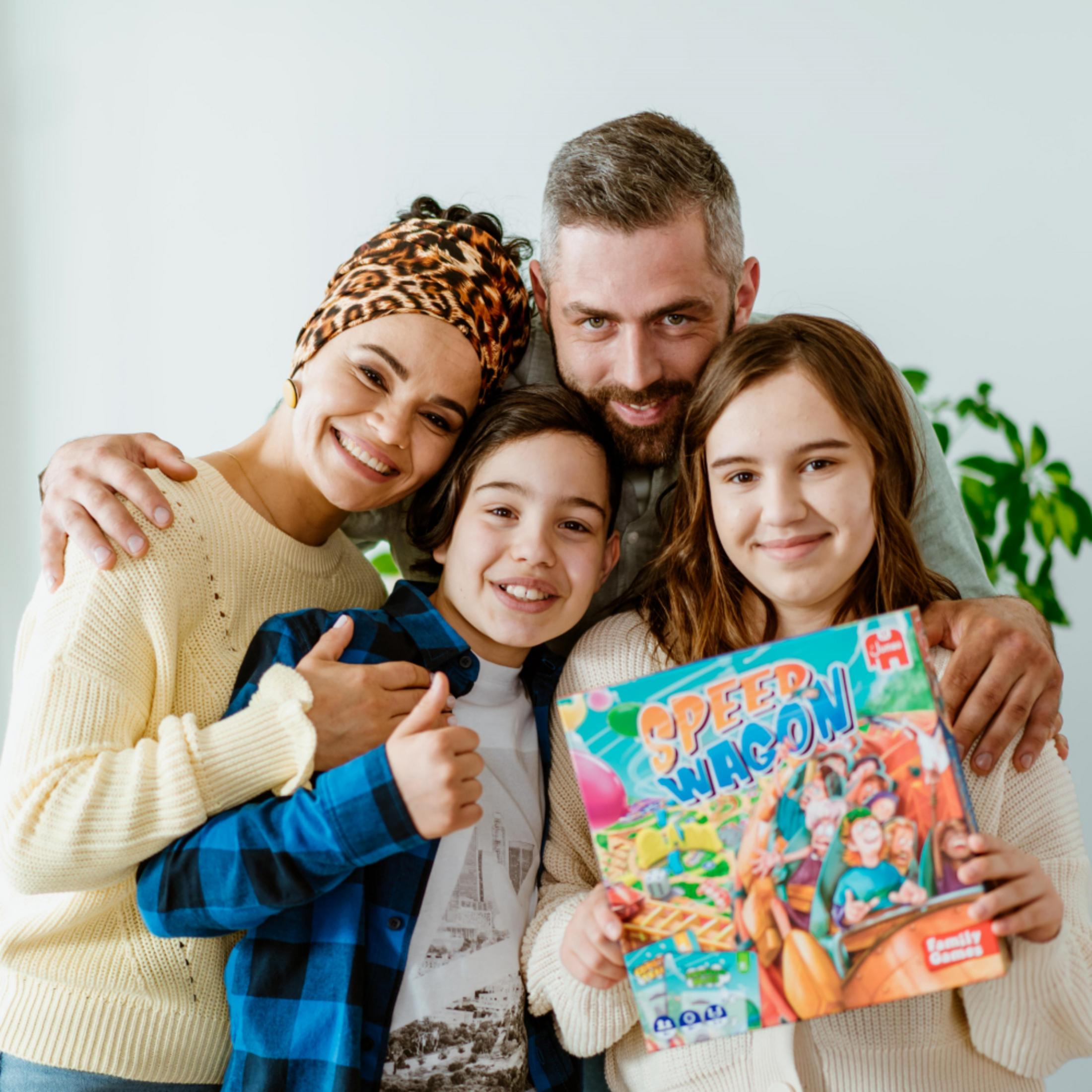 Una familia sonríe y sostiene la caja de un juego de mesa "Speed Wagon".