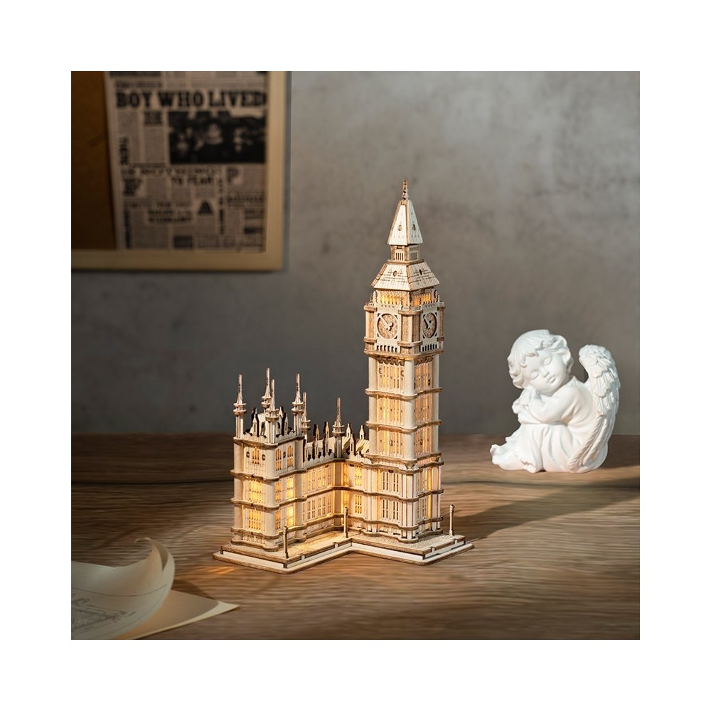 Detaylı Big Ben modeli, küçük bir melek heykelinin yanında ahşap bir masada duruyor.