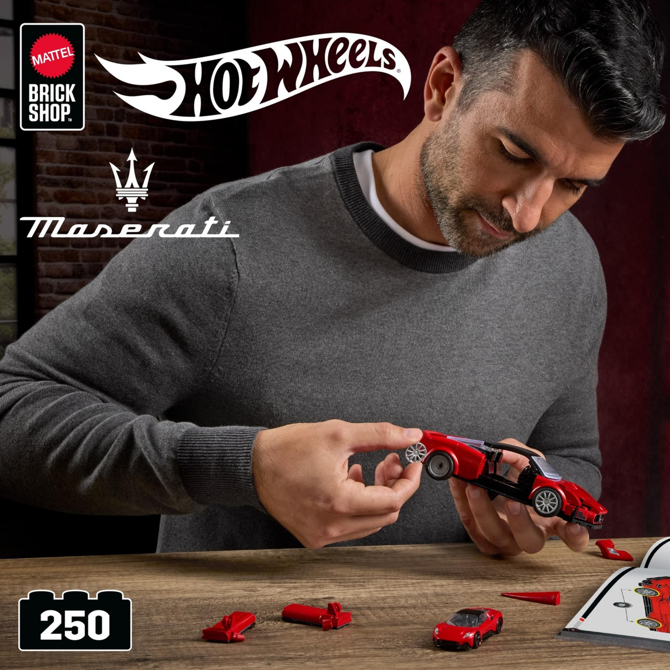Uomo assembla kit Maserati Hot Wheels rosso. Istruzioni e pezzi sul tavolo.