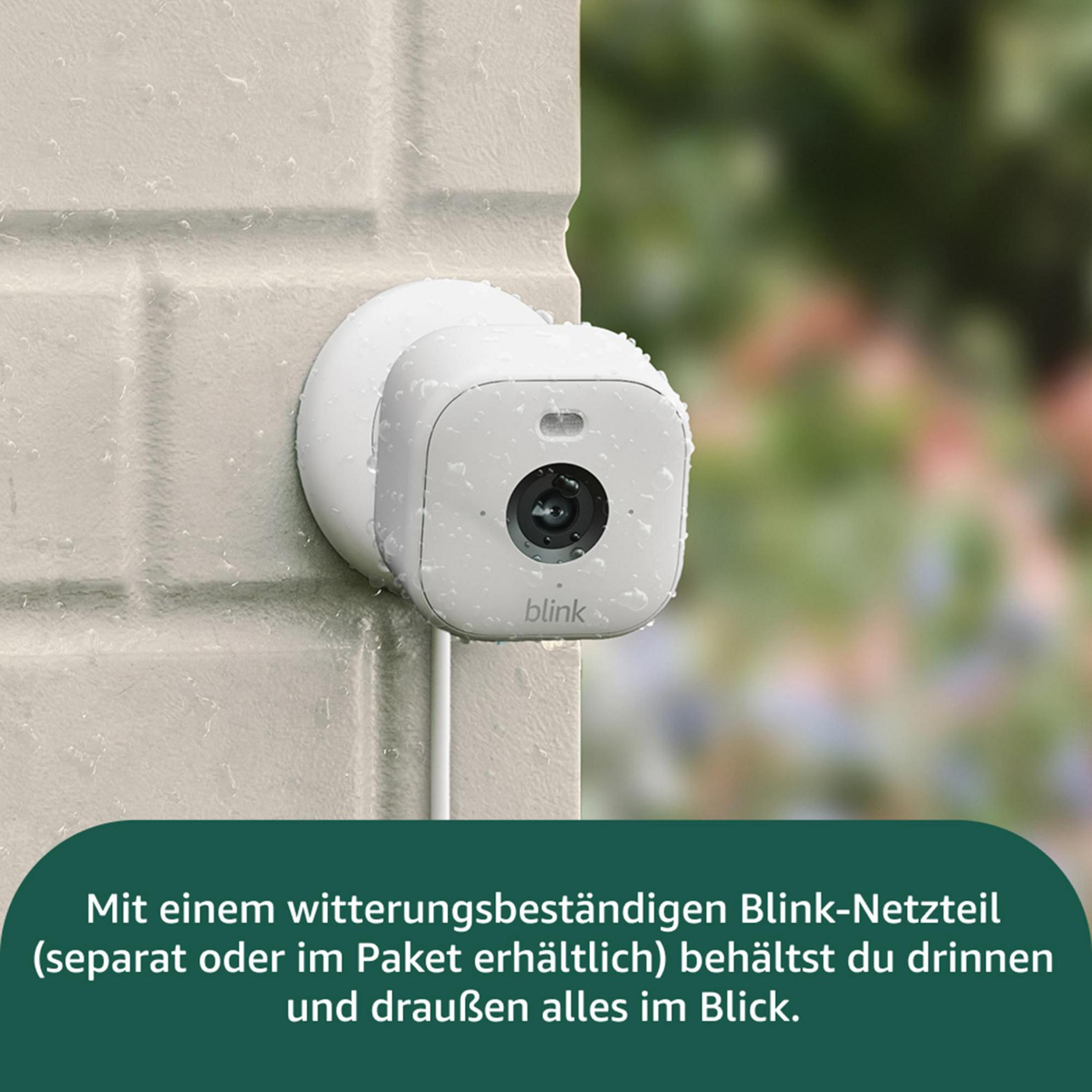 Eine weiße Blink-Kamera hängt an einer Wand, mit Regentropfen bedeckt.