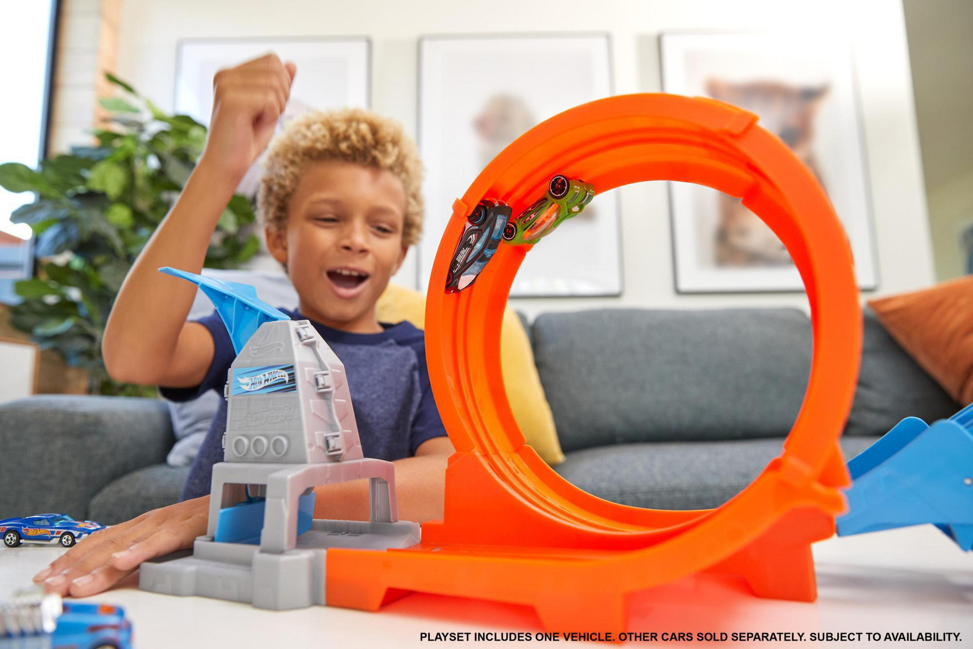 Junge spielt mit Hot Wheels-Rennstrecke mit zwei Autos in einer Schleife.