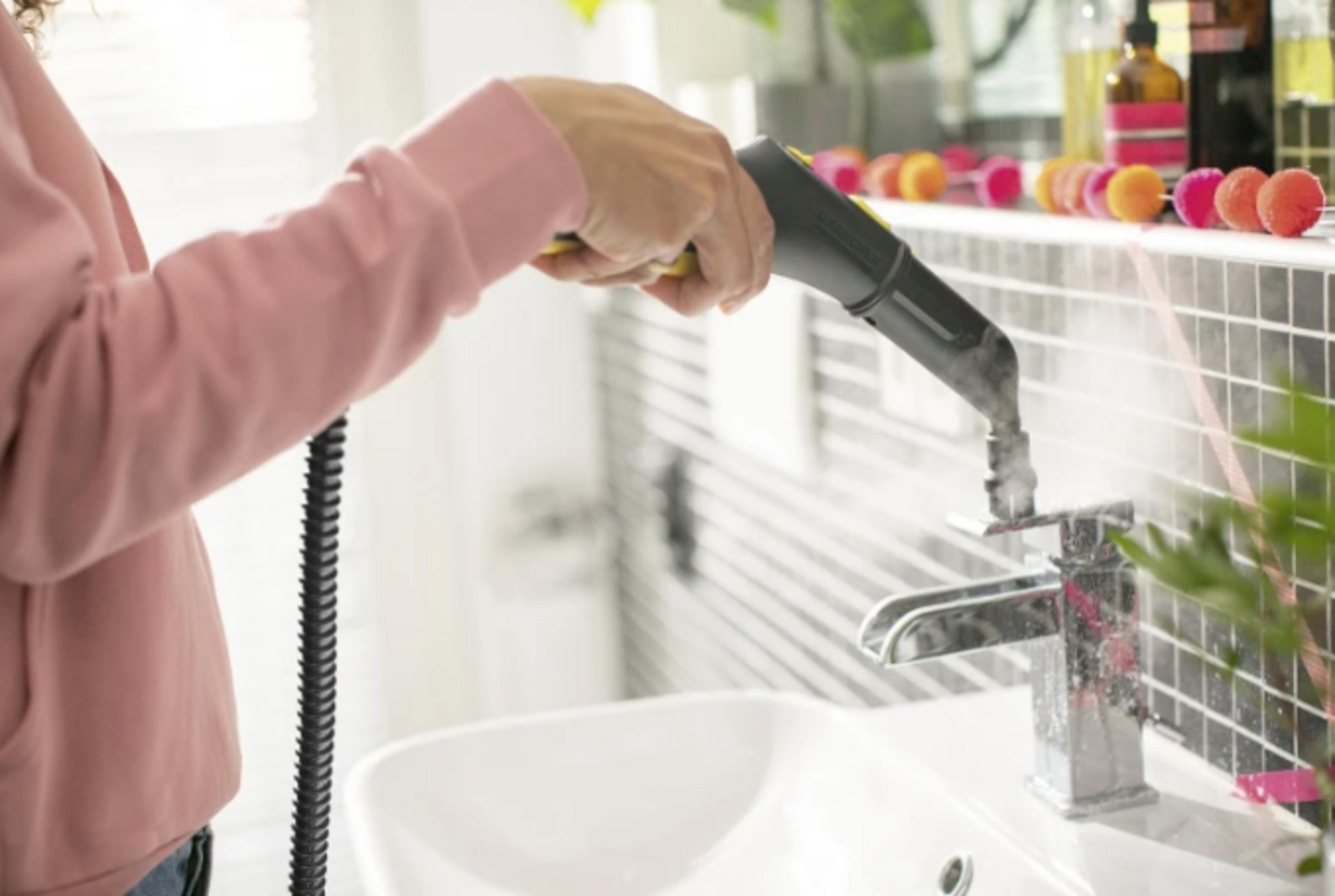 Persona che pulisce un rubinetto con pulitore a vapore in un bagno.