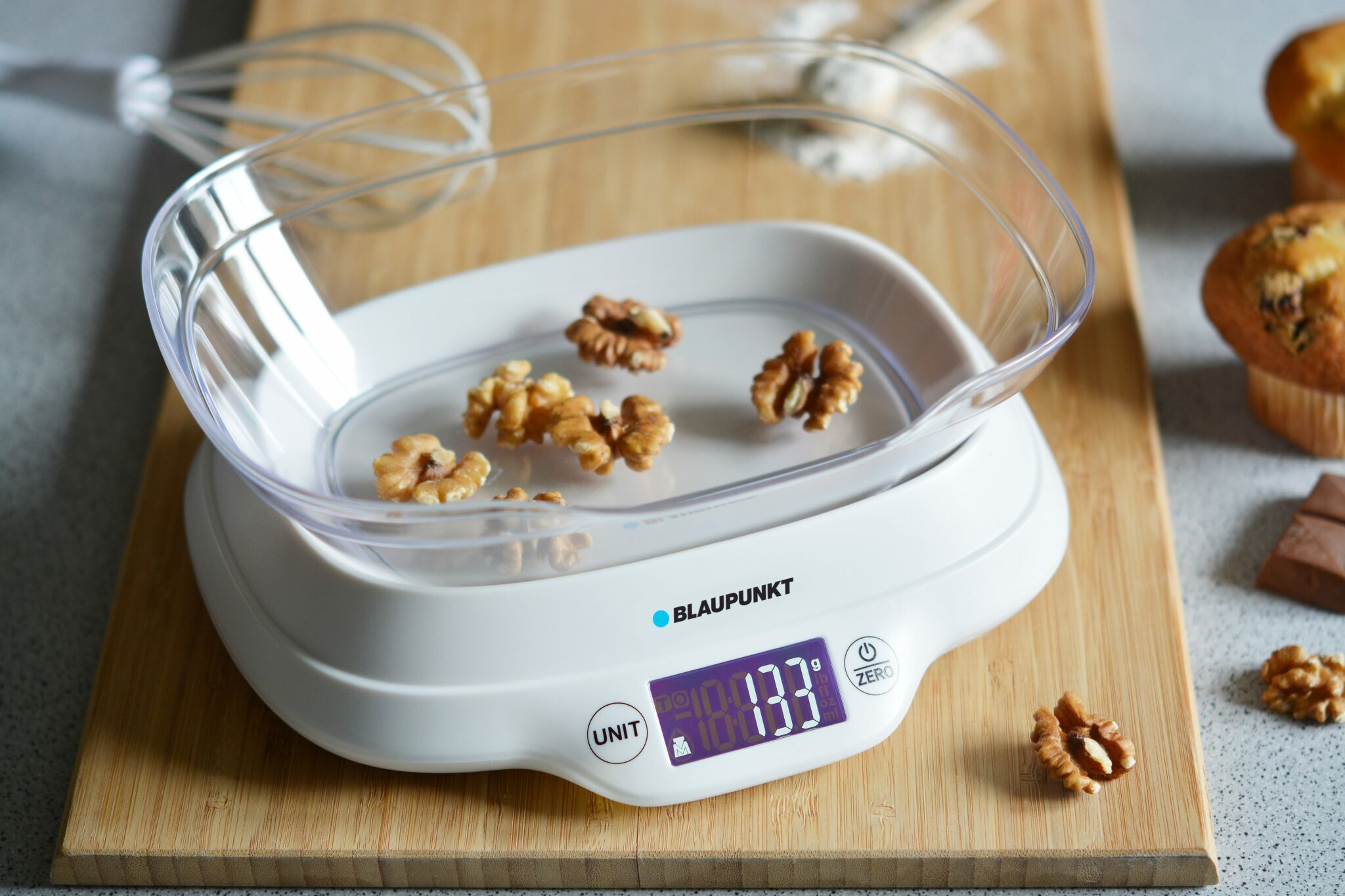 Una báscula de cocina digital con nueces en el bol y sobre la tabla.