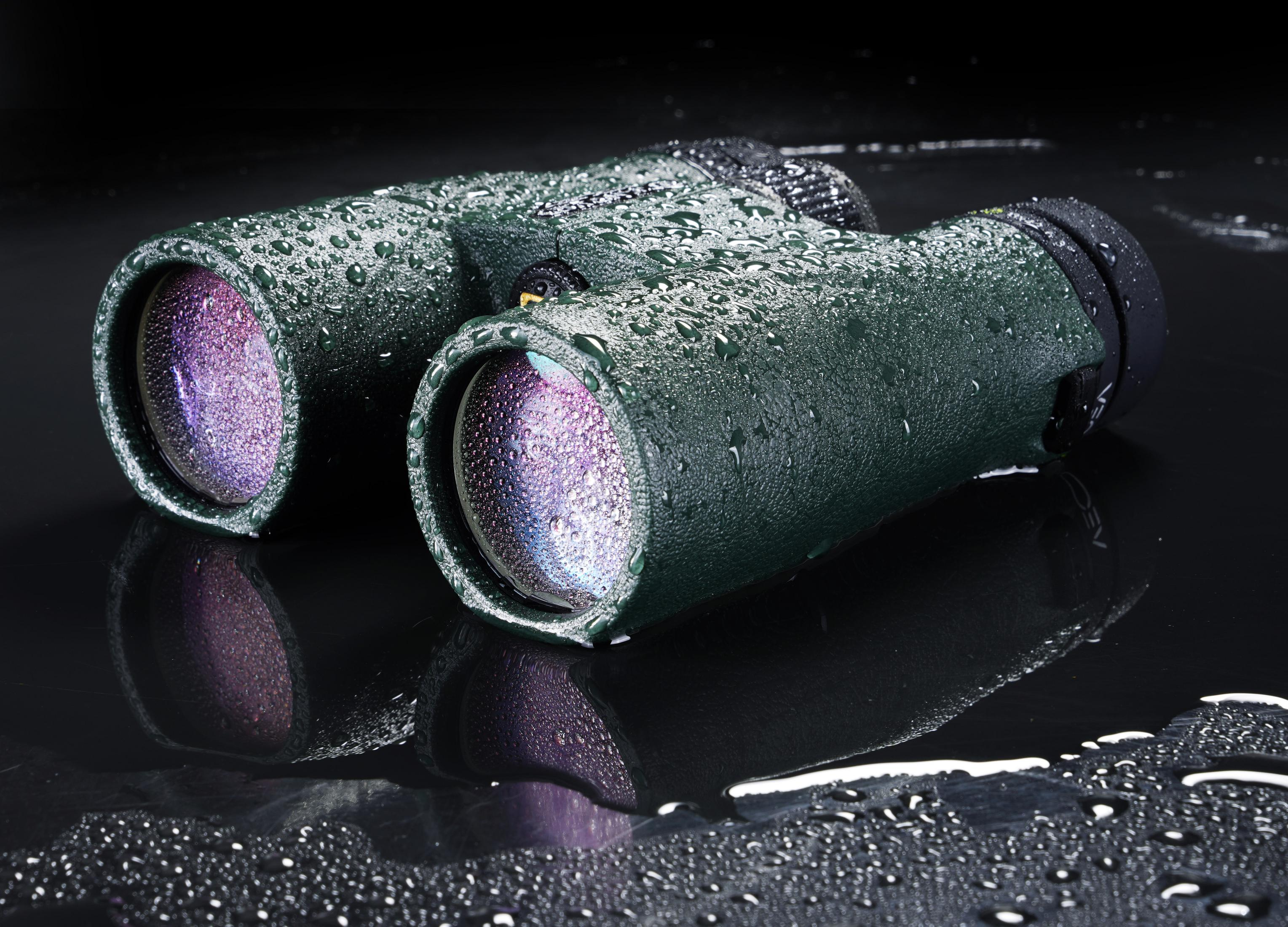 Binoculares verdes con gotas de agua sobre fondo negro.