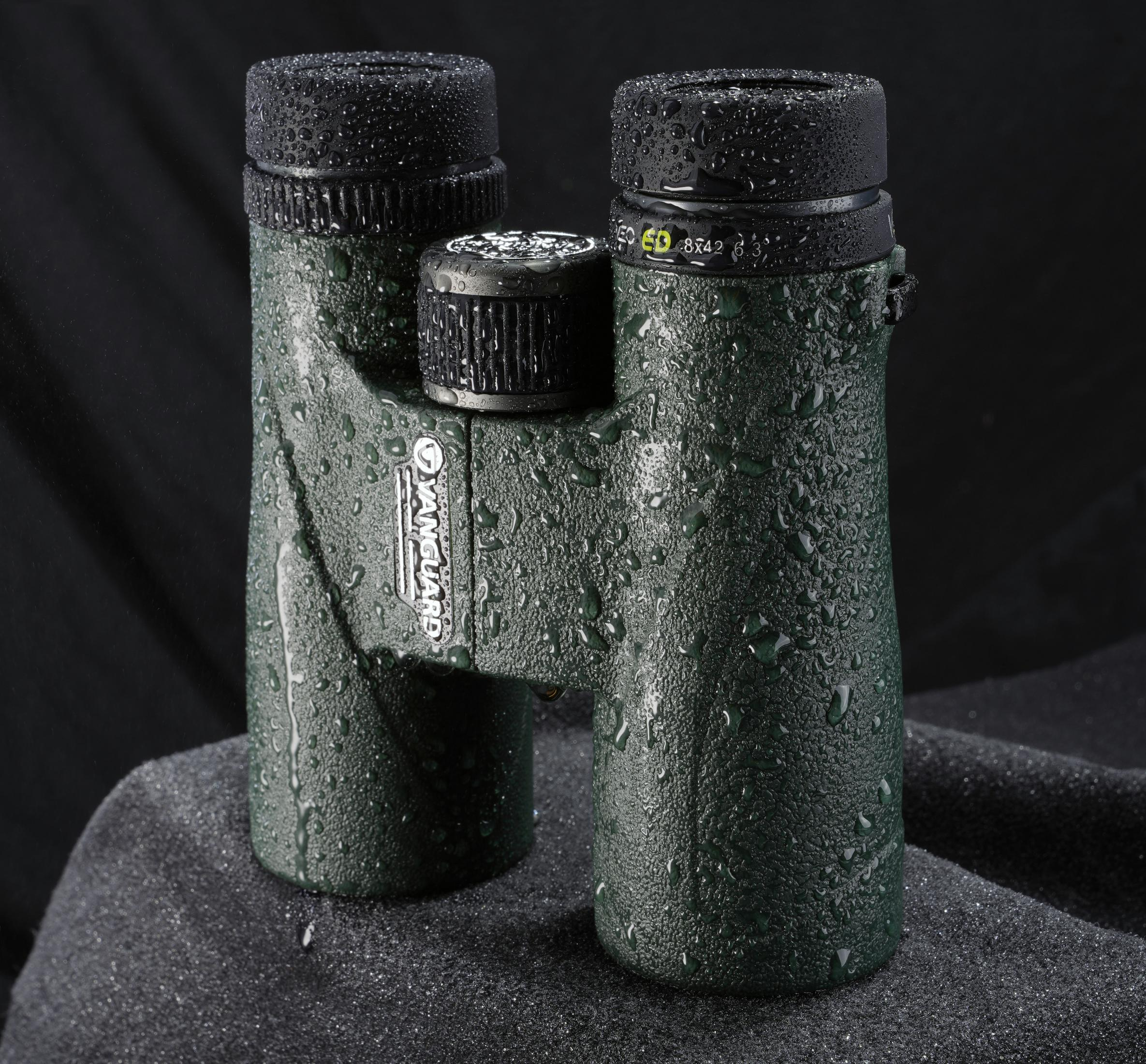 Prismáticos verdes cubiertos de gotas de agua sobre fondo negro.
