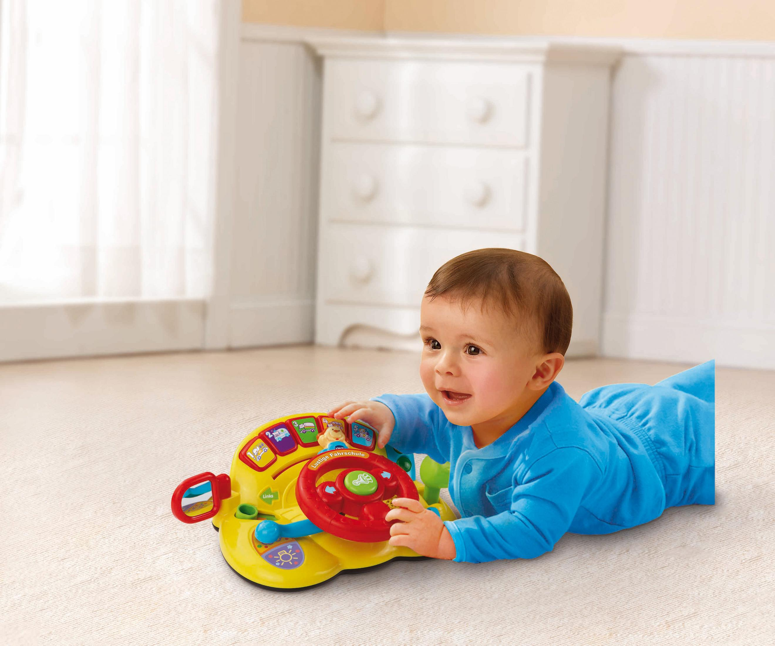 Ein Baby in einem blauen Strampler liegt auf dem Bauch und spielt mit einem gelben Lenkrad-Spielzeug.