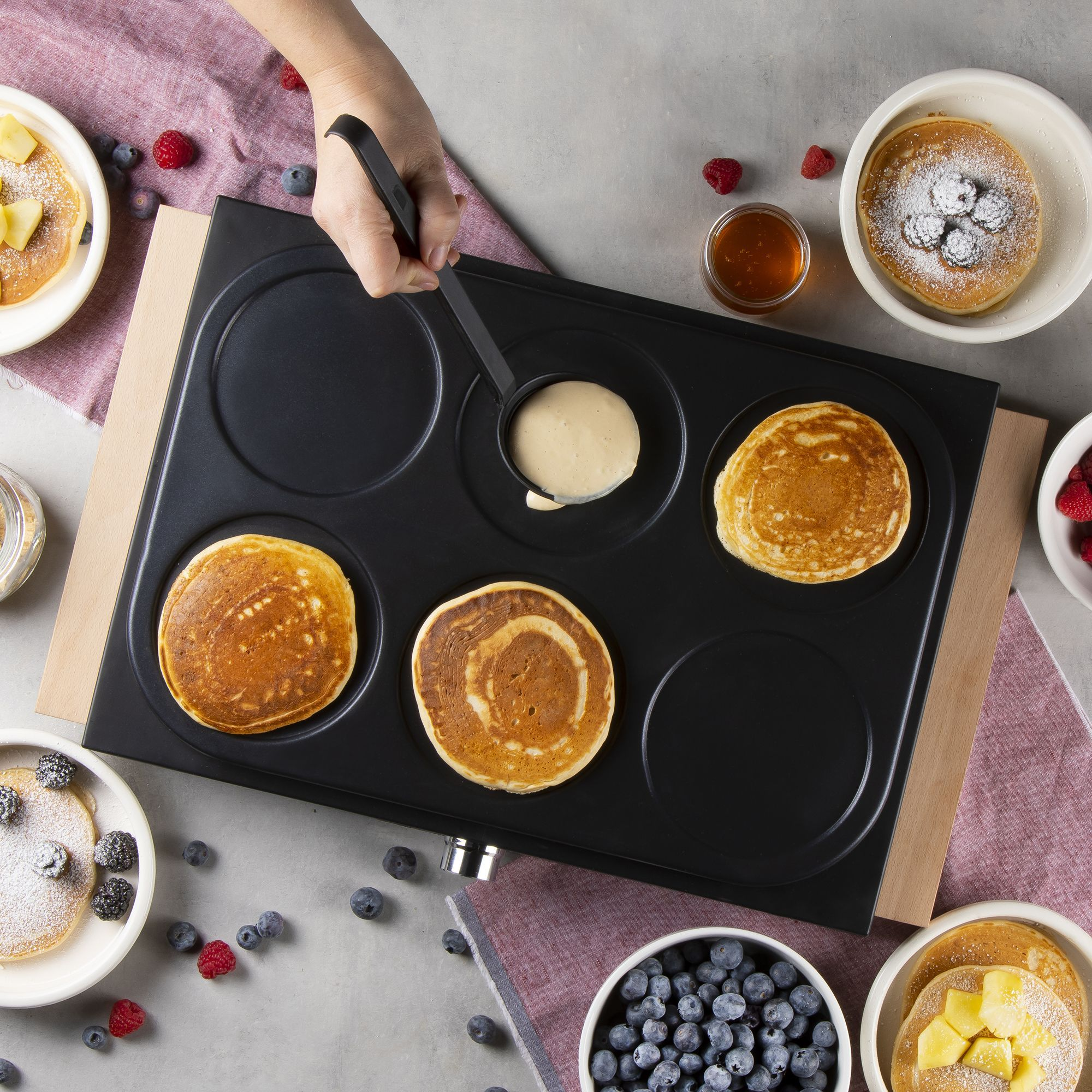 Pancakes werden auf einer elektrischen Grillplatte gebacken, garniert mit Beeren und Puderzucker.