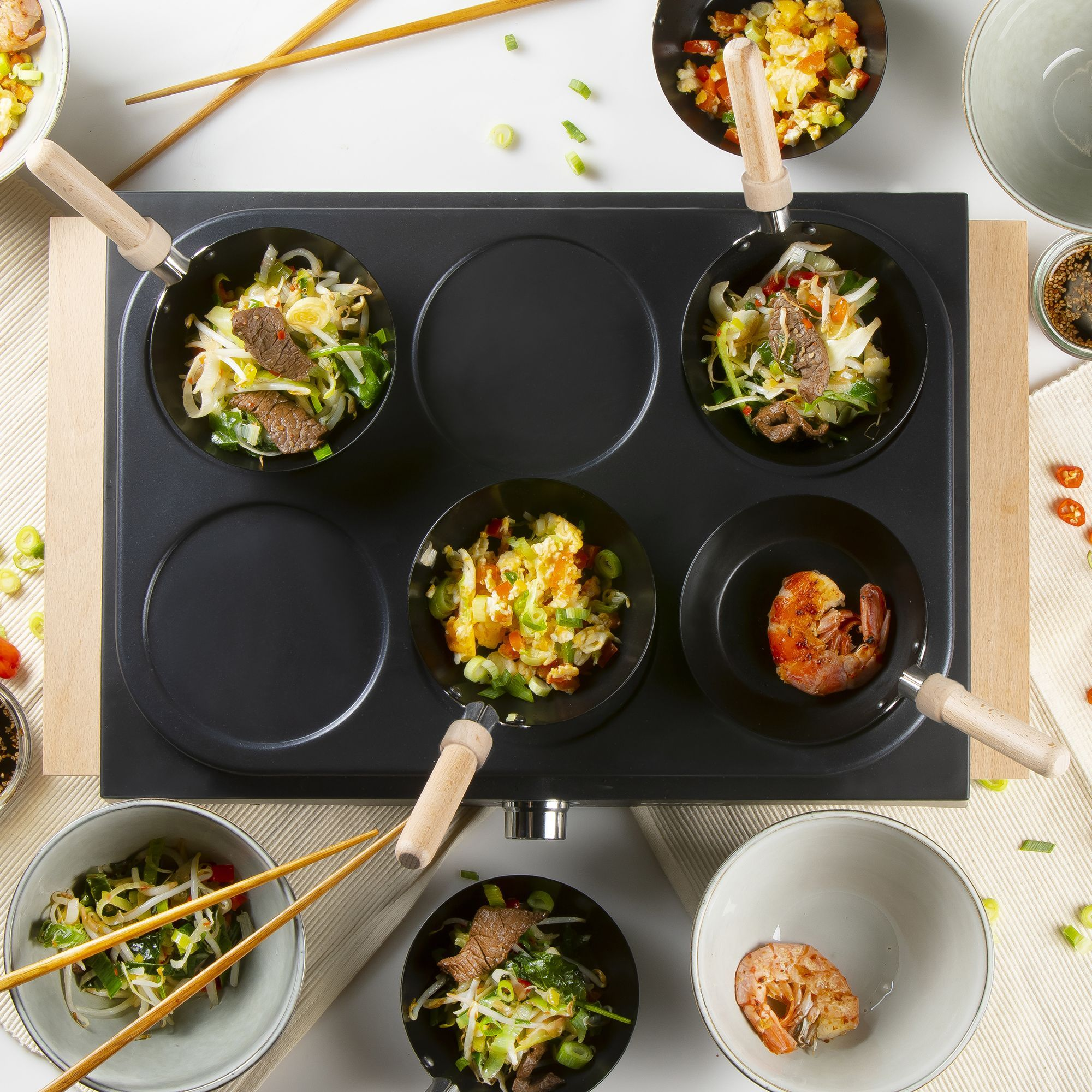 Sechs Mini-Woks mit Essen auf einem Grill. Ein Wok enthält Garnelen.