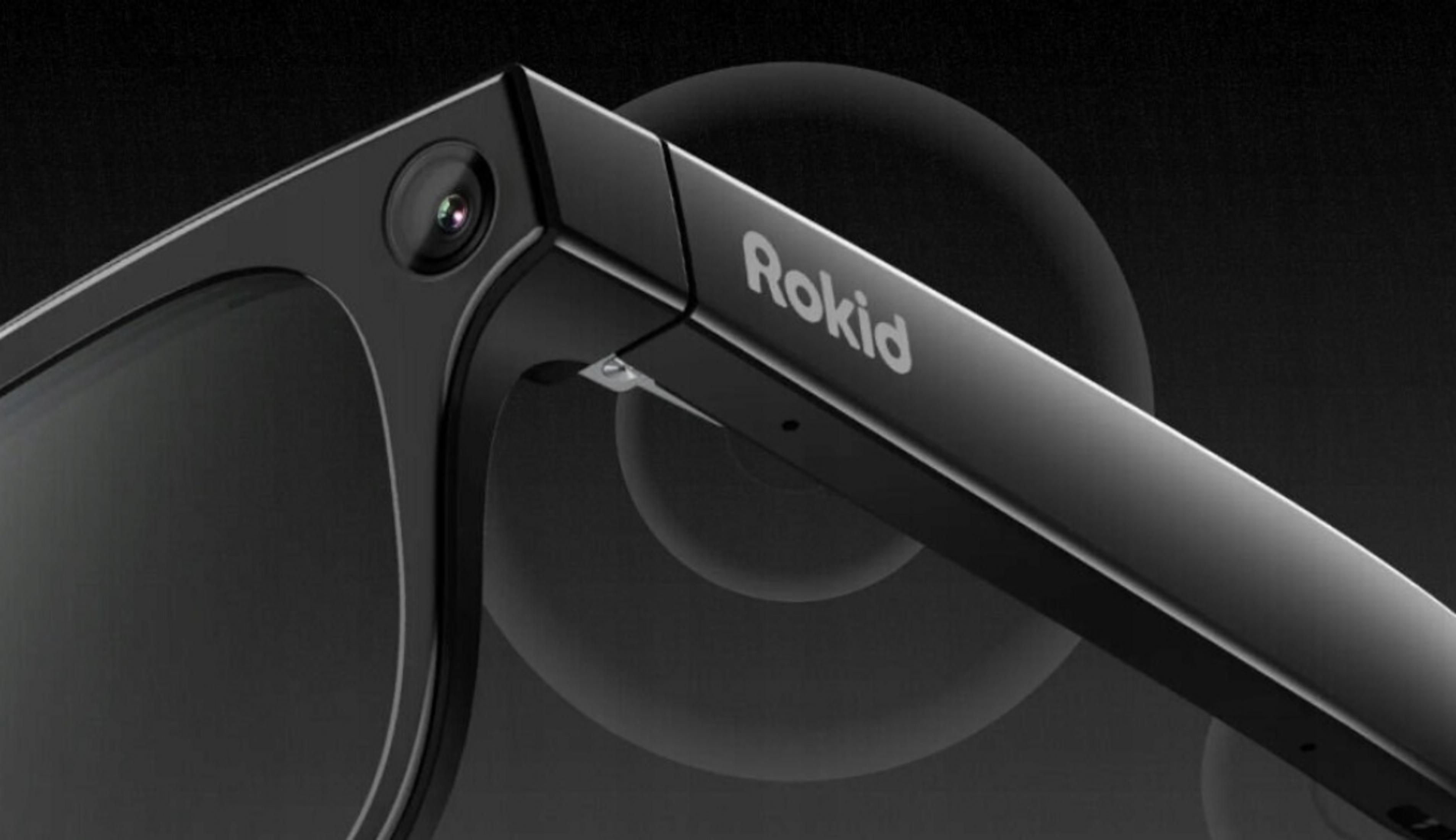 Gafas AR Rokid negras con cámara y logo plateado sobre fondo oscuro.