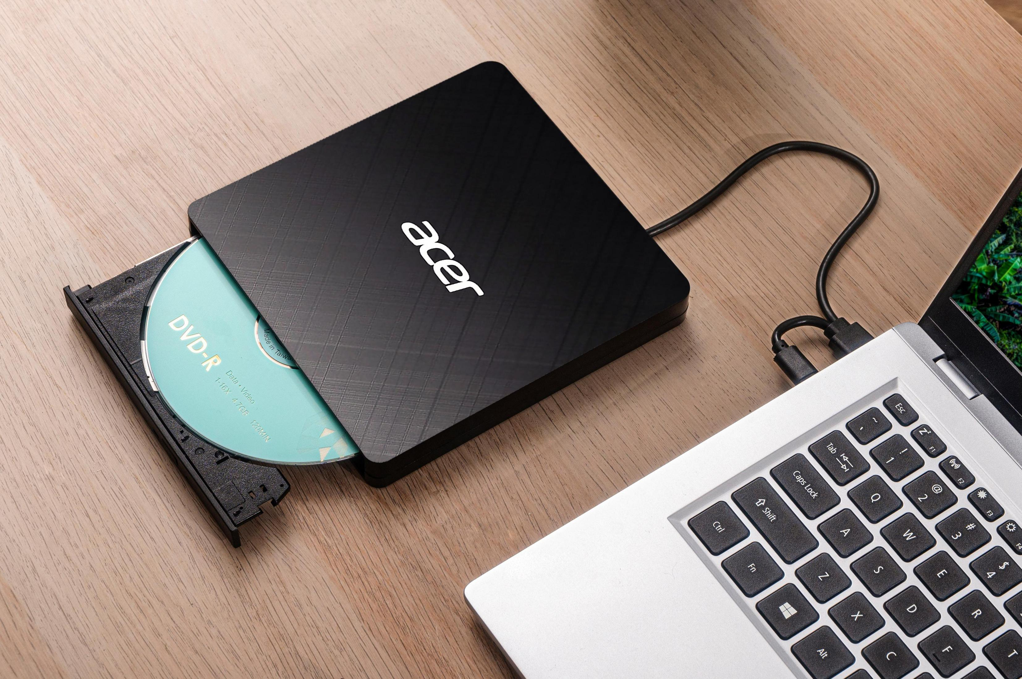 Czarna zewnętrzna nagrywarka DVD Acer z włożoną płytą DVD-R obok laptopa.