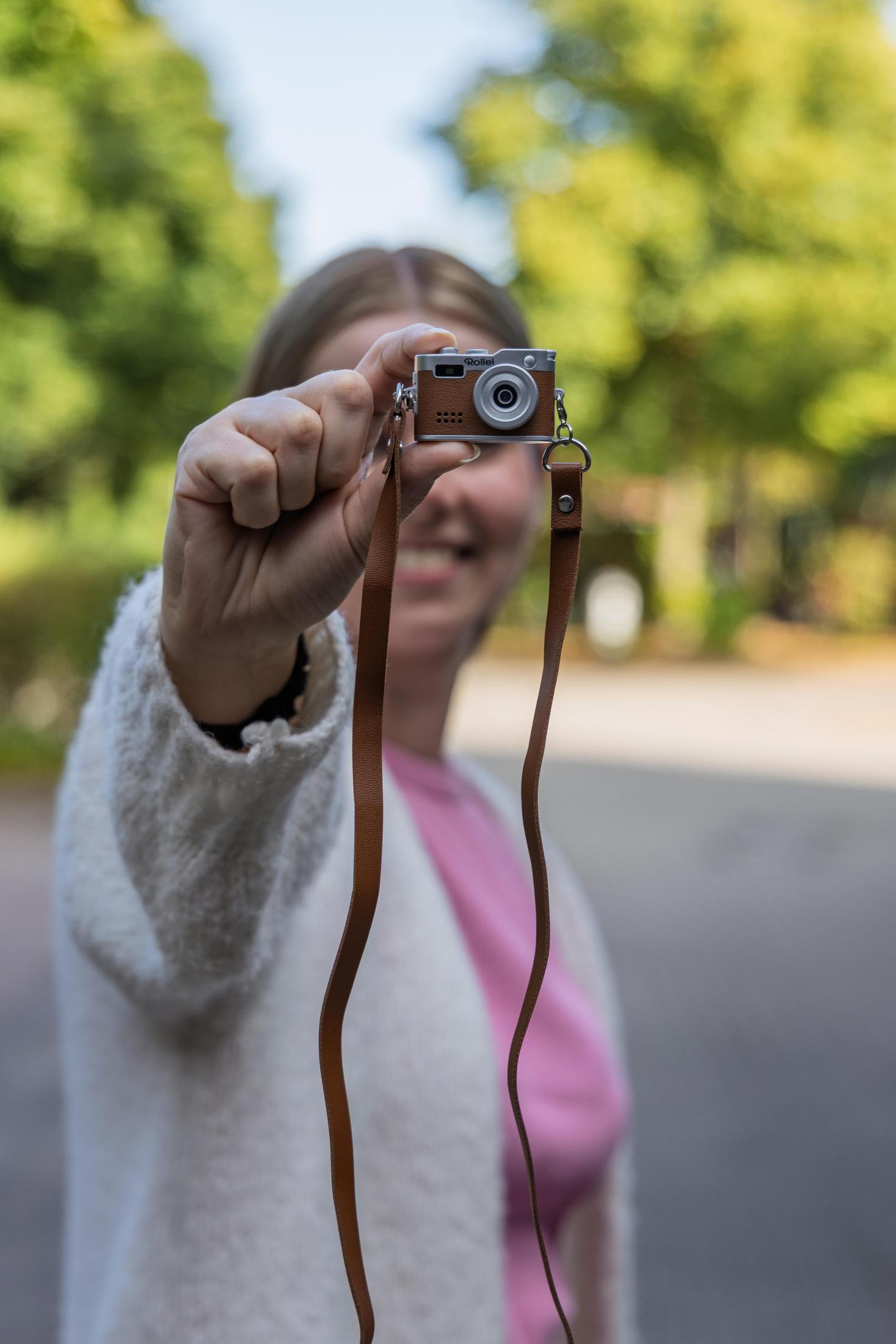 Una persona tiene in mano una piccola fotocamera digitale argento e marrone con tracolla in pelle.