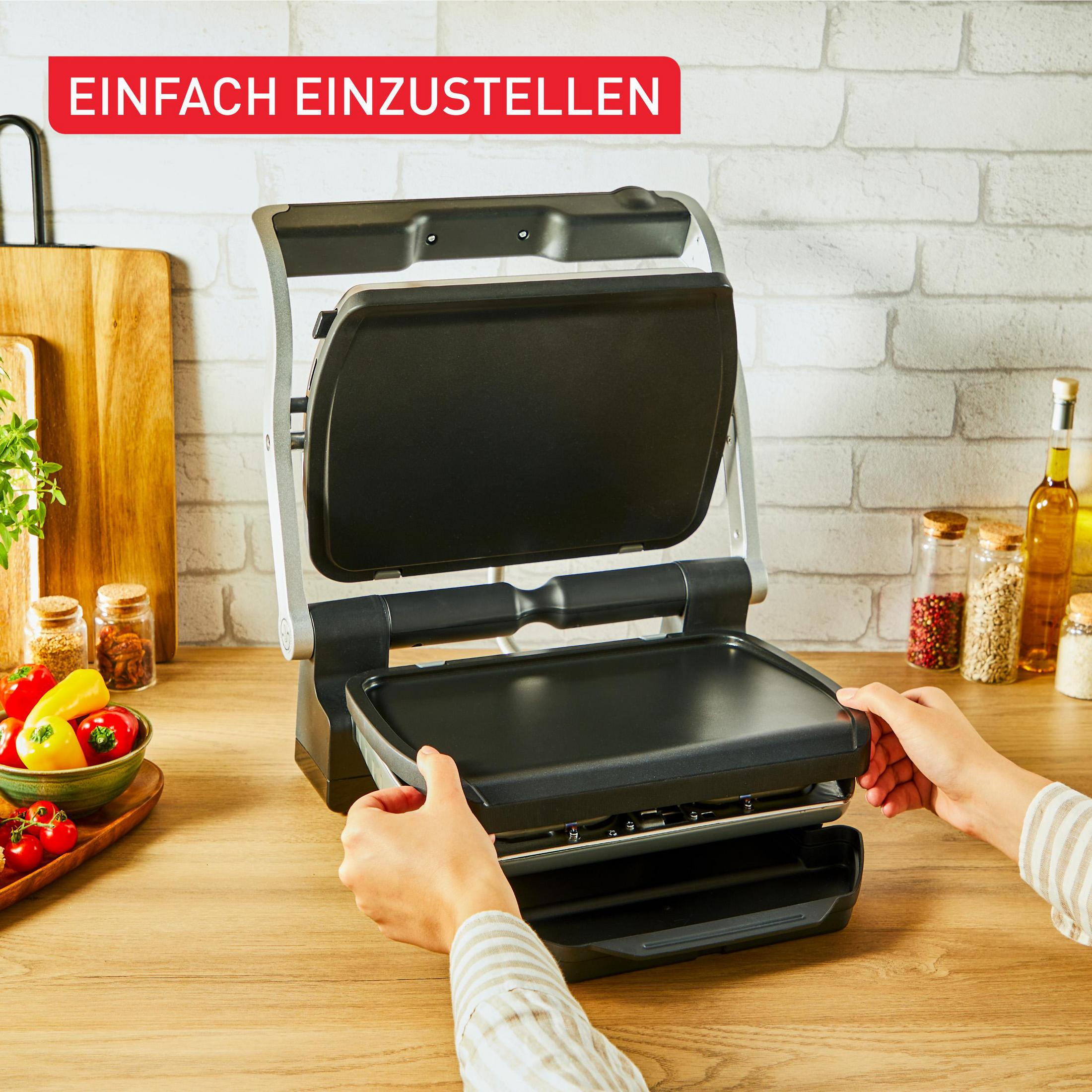 Eine Person stellt eine offene Kontaktgrillplatte auf einem Holztisch ein.