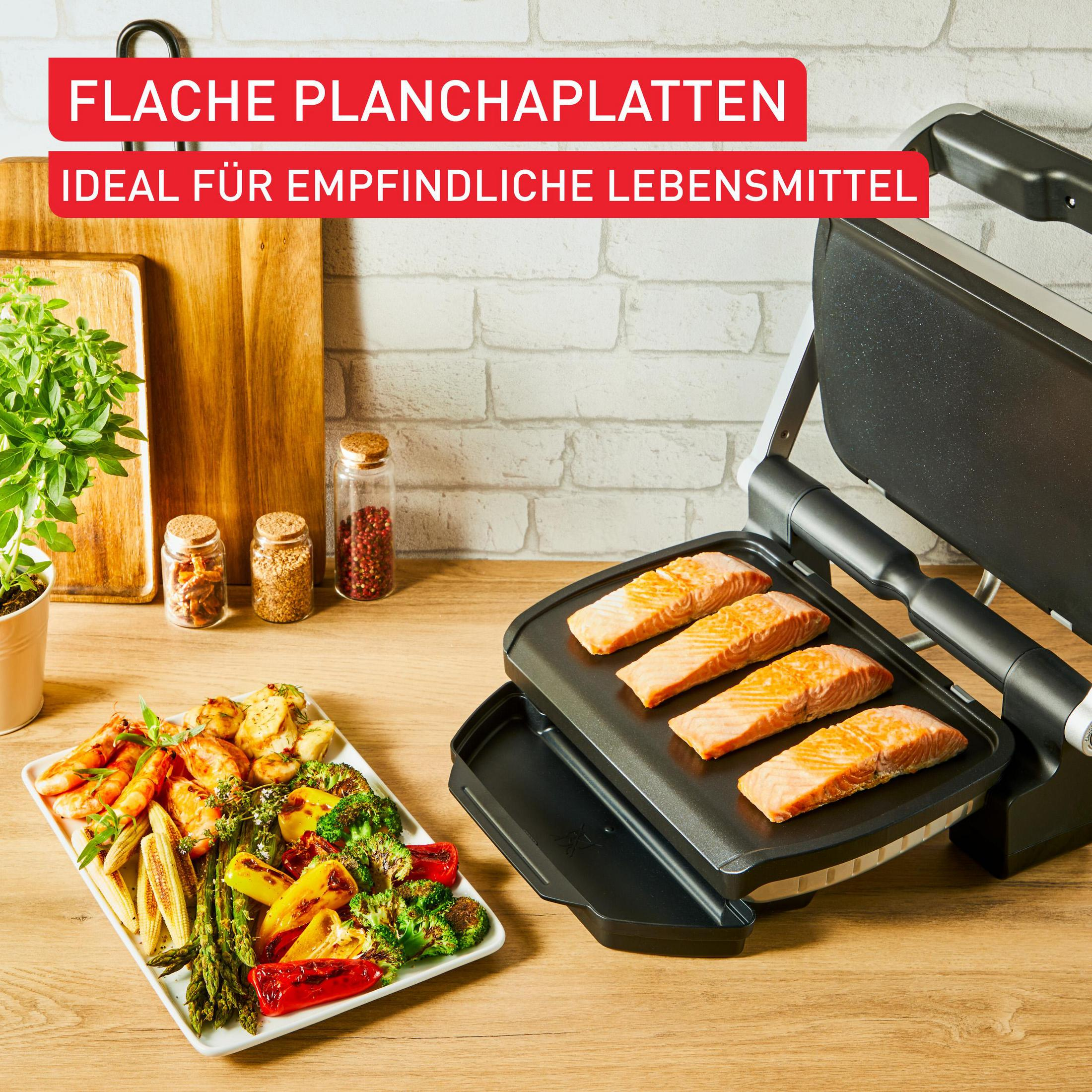 Vier Lachsfilets auf einer Grillplatte, daneben ein Teller mit gegrilltem Gemüse und Garnelen.
