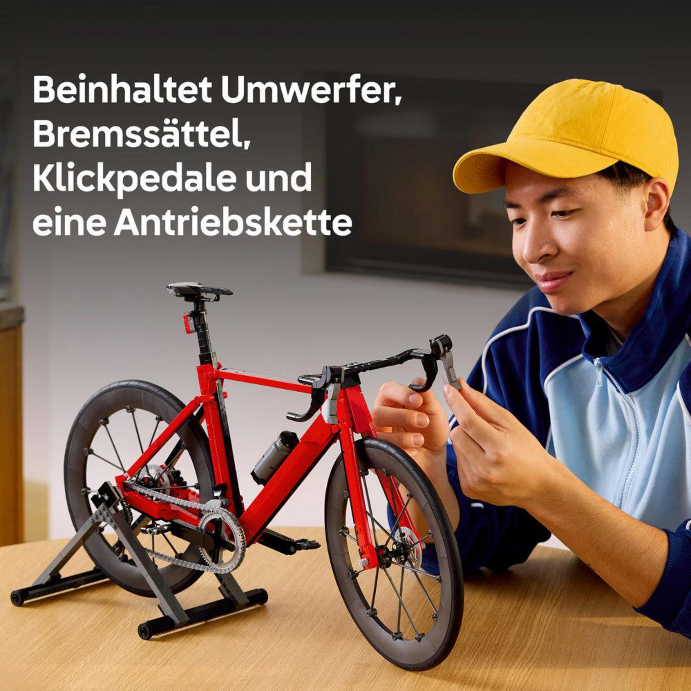 Un hombre con gorra amarilla monta una bicicleta de carreras roja de Lego en una mesa.