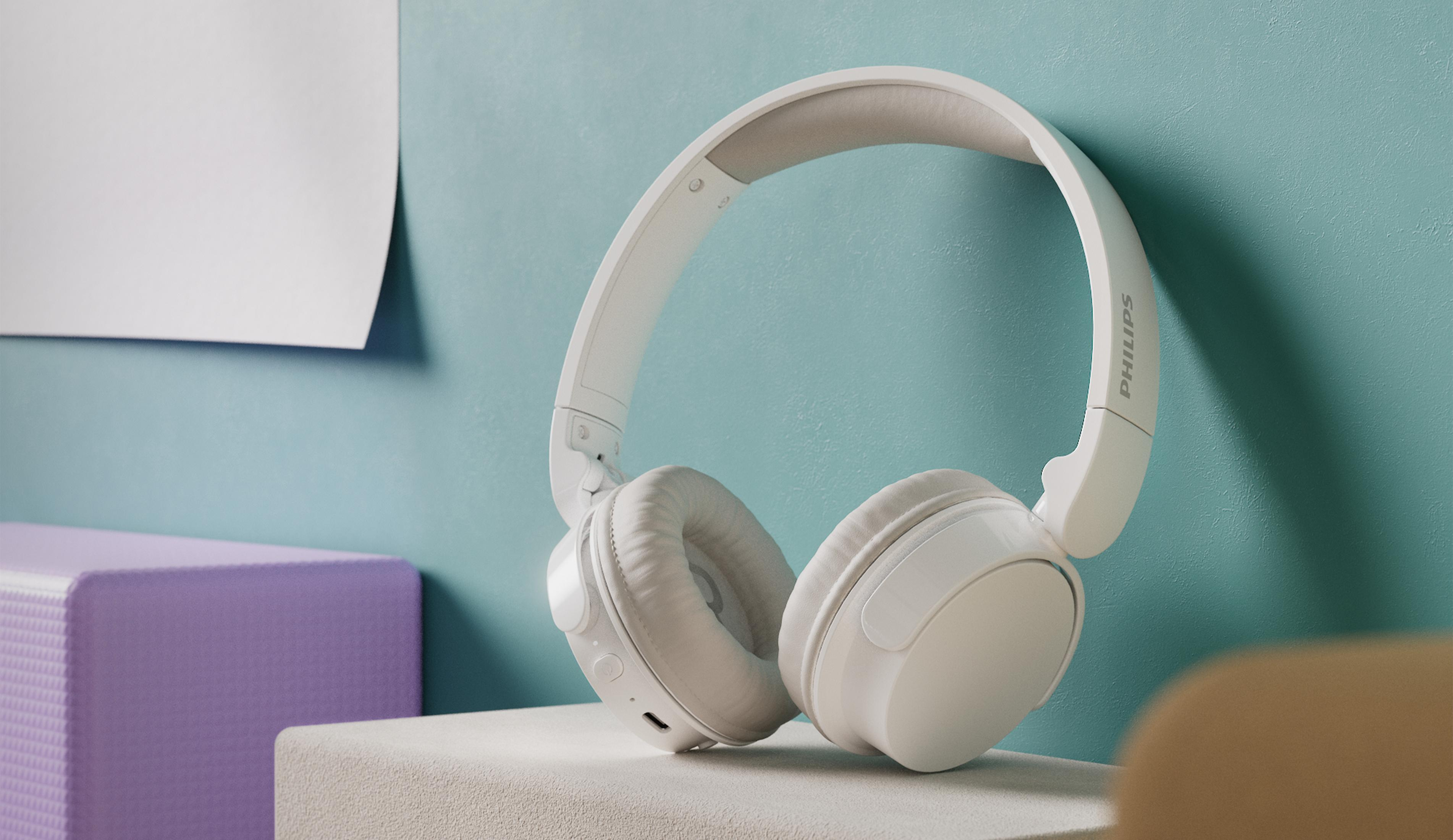 Auriculares Philips blancos descansan sobre una superficie clara frente a una pared turquesa.