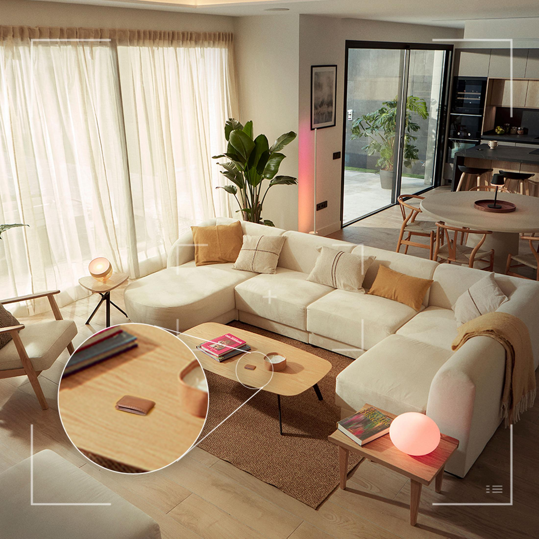Una sala de estar luminosa con sofá seccional, mesa de centro, plantas y cocina abierta.