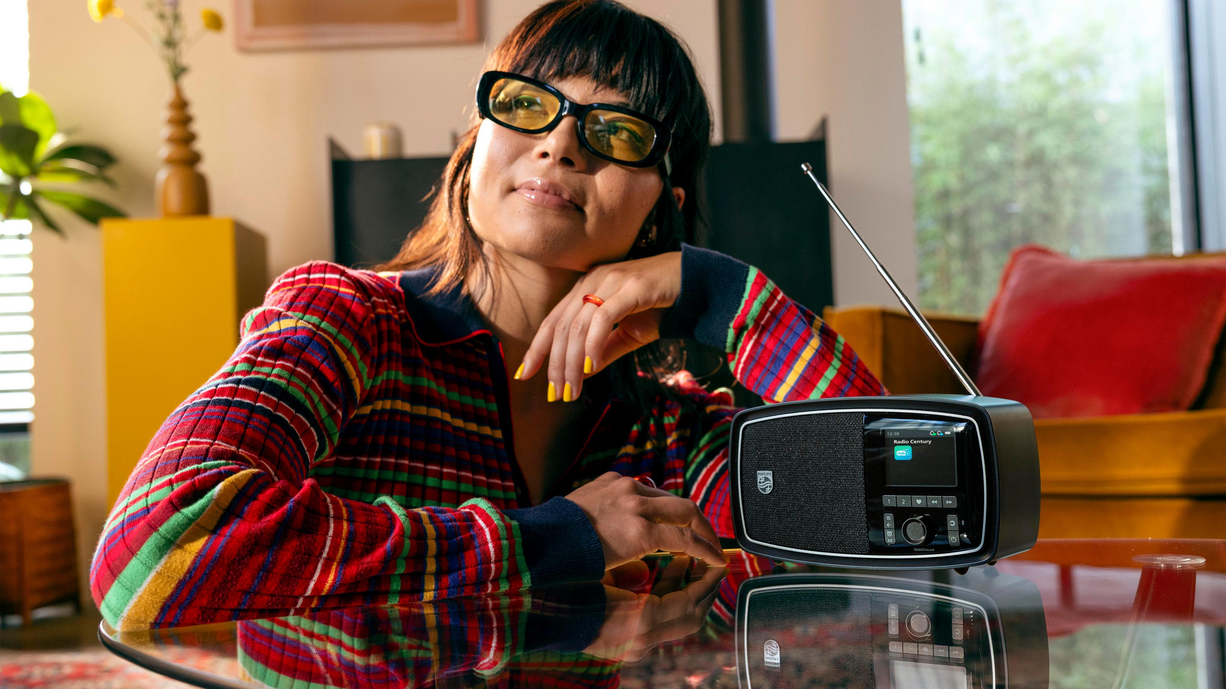 Une femme portant des lunettes est assise à une table avec une radio.