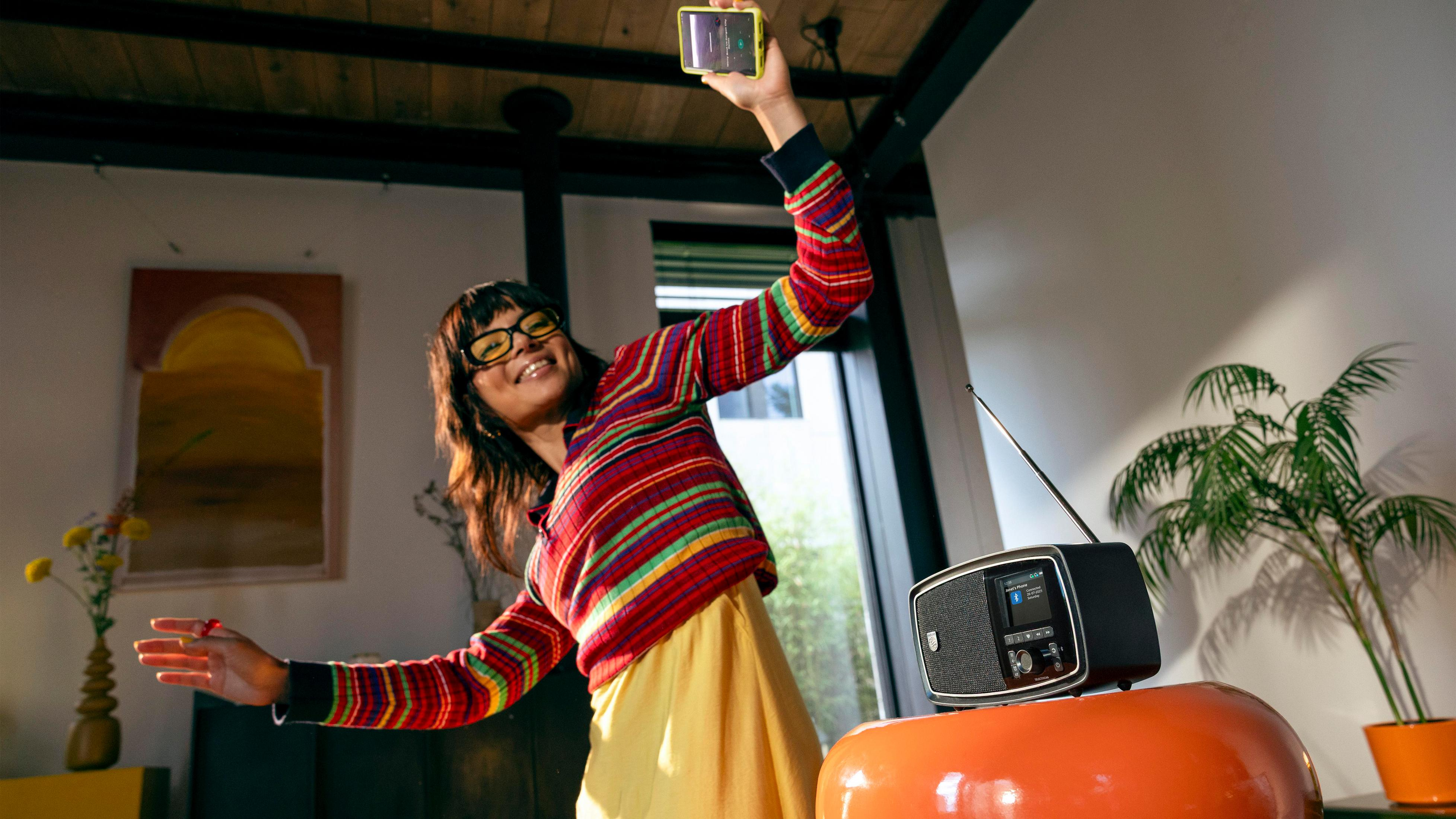 Une femme lunettes danse près d'une radio, tenant un smartphone.