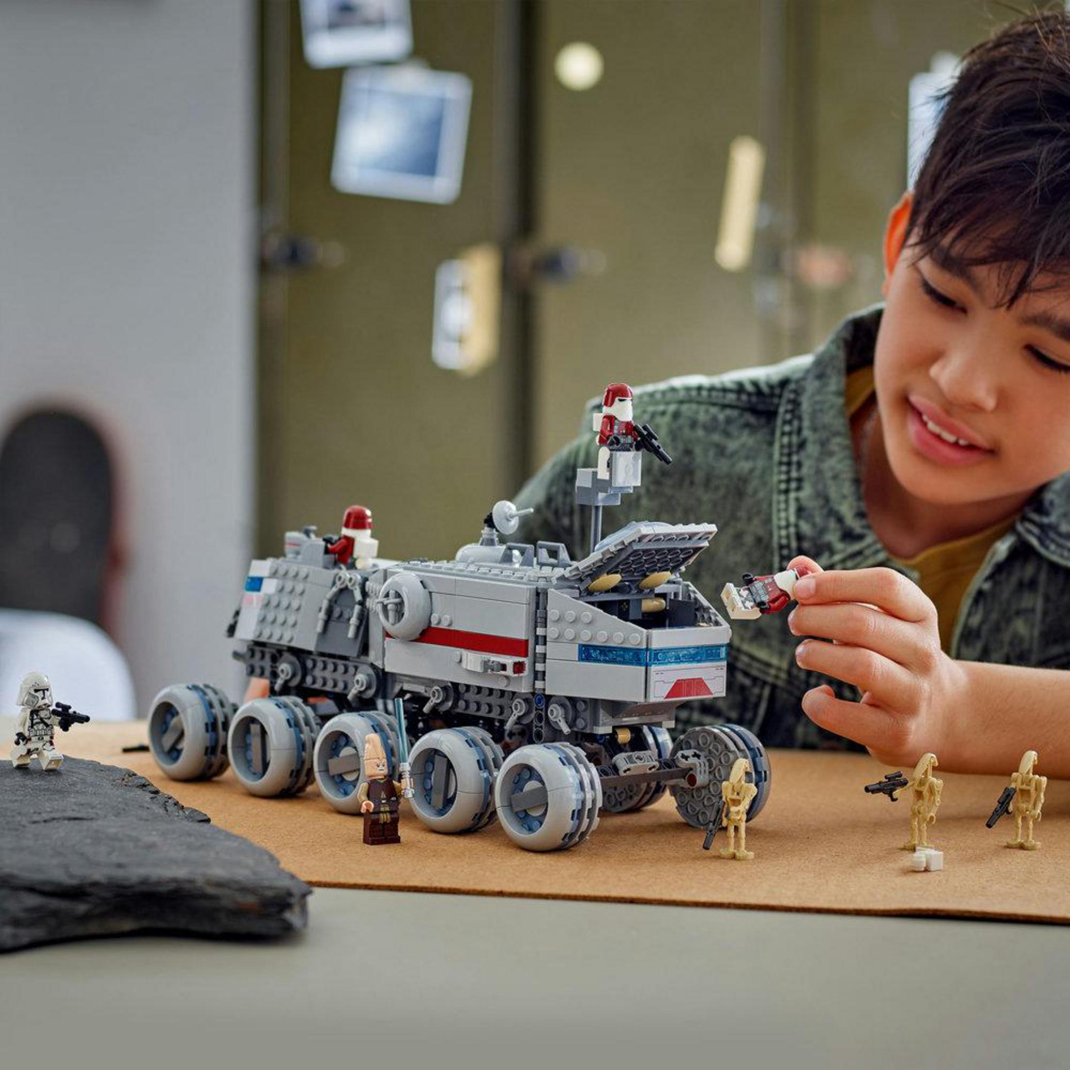 Un ragazzo costruisce un veicolo Lego grigio con accenti rossi e figure.