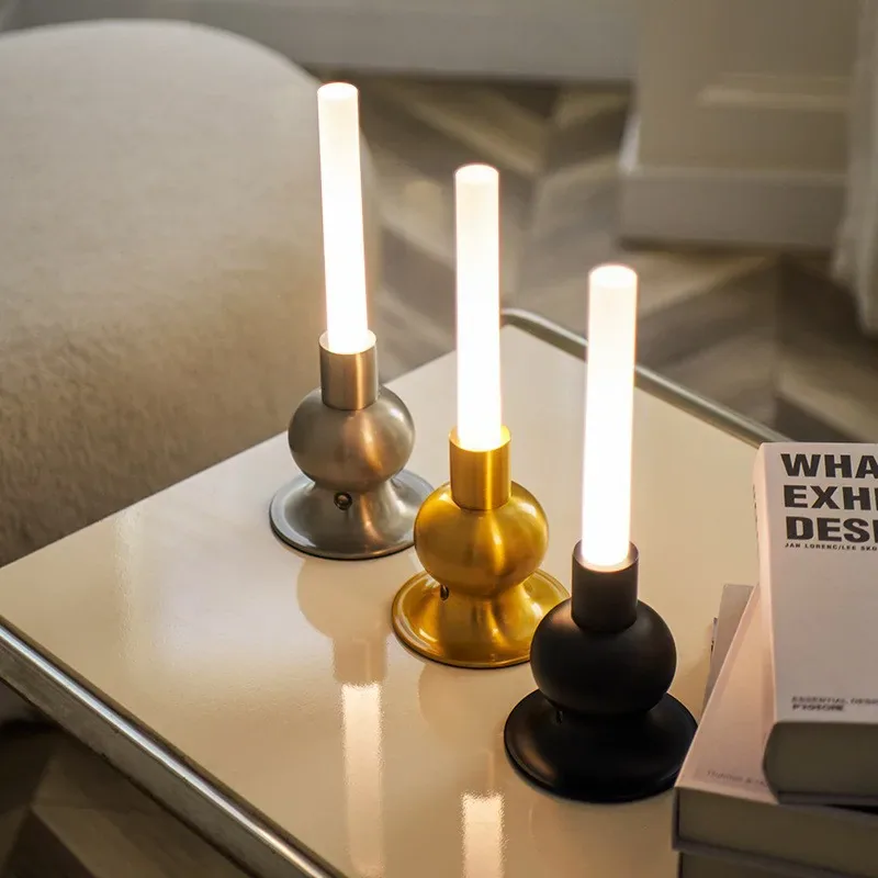 Drei moderne LED-Lampen in Silber, Gold und Schwarz stehen neben Büchern auf einem Tisch.