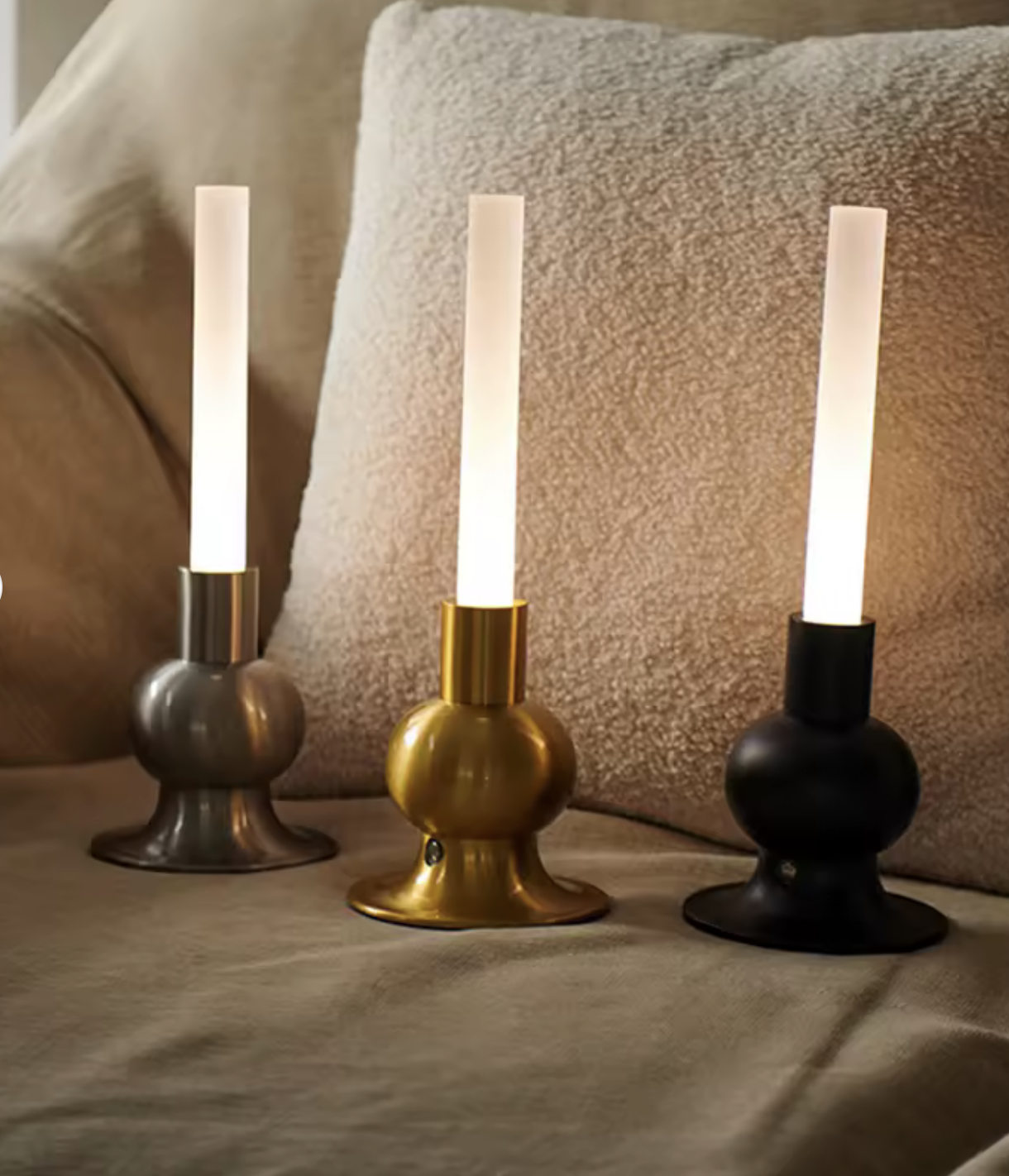 Drei moderne Tischlampen in Silber, Gold und Schwarz auf einem Sofa.