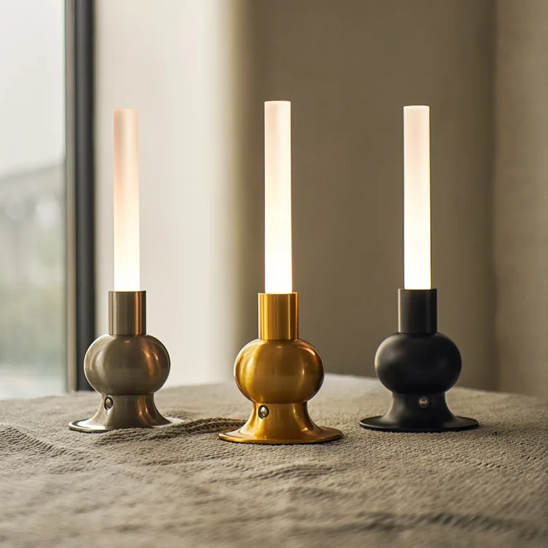 Drei moderne Tischlampen mit mattweißen Röhren und metallischen Sockeln in Grau, Gold und Schwarz.