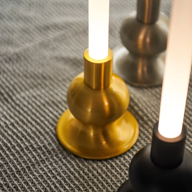 Drei moderne Lampen mit goldenem, silbernem und schwarzem Sockel auf einer gestreiften Decke.