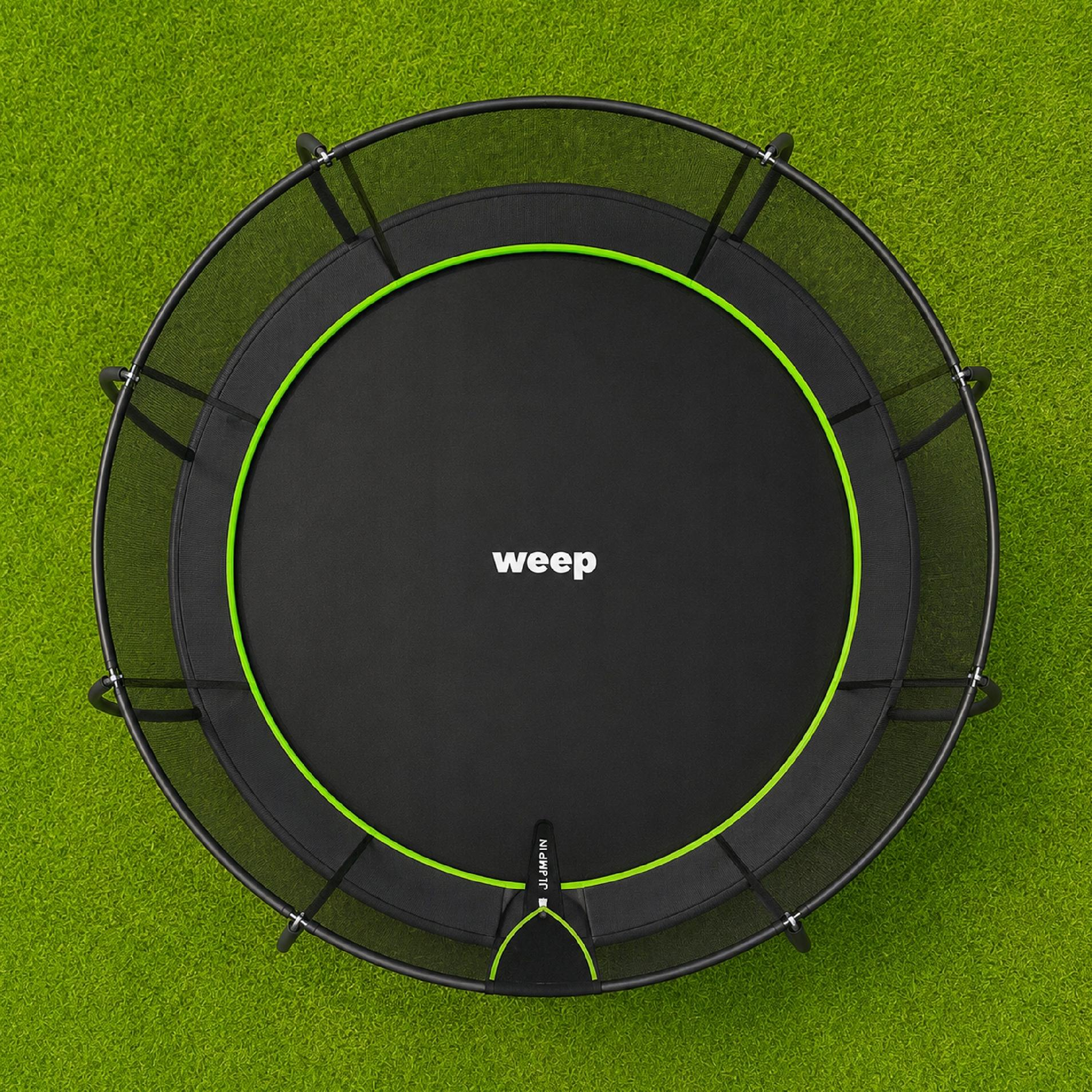 Okrągły trampolin z czarną matą i siatką zabezpieczającą na zielonej trawie.