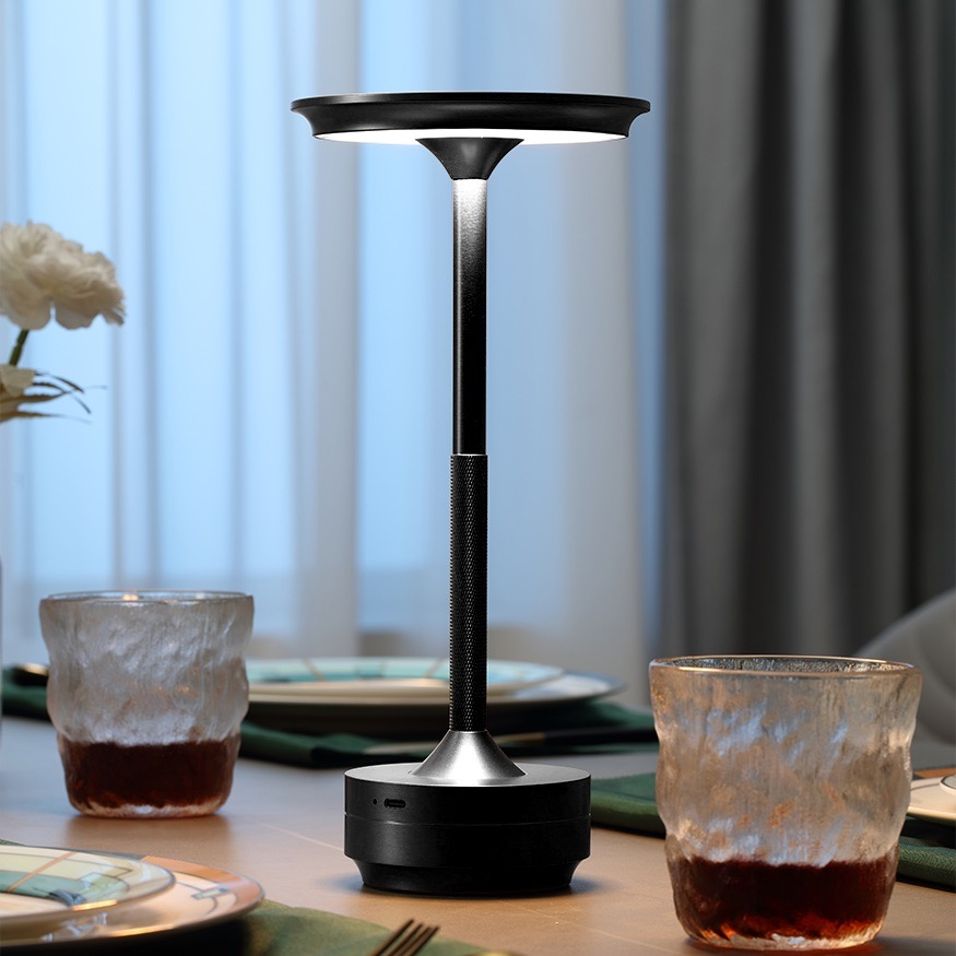 Eine moderne schwarze Tischlampe mit silbernem Ständer steht auf einem Holztisch mit Gläsern.