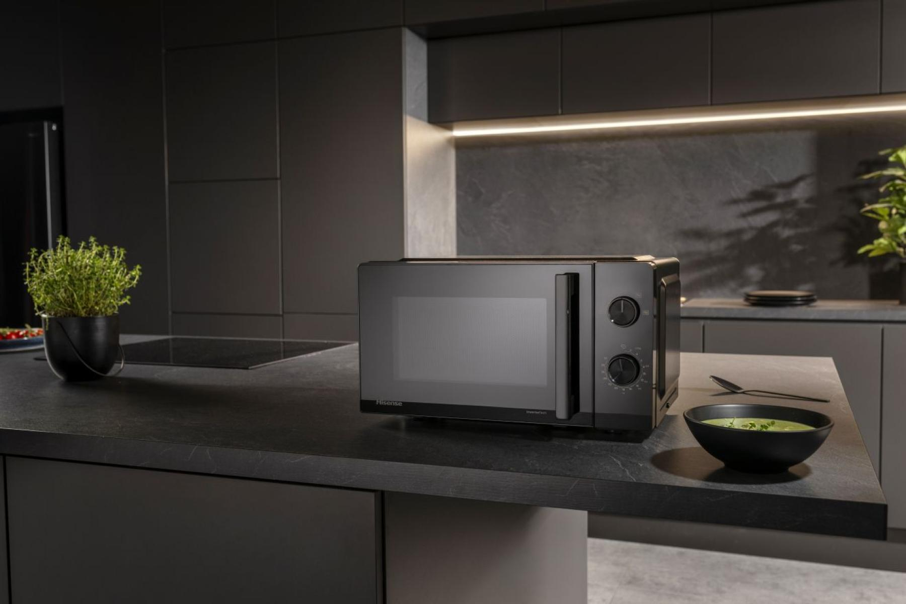 Un forno a microonde nero si trova su un bancone scuro accanto a una ciotola di zuppa.
