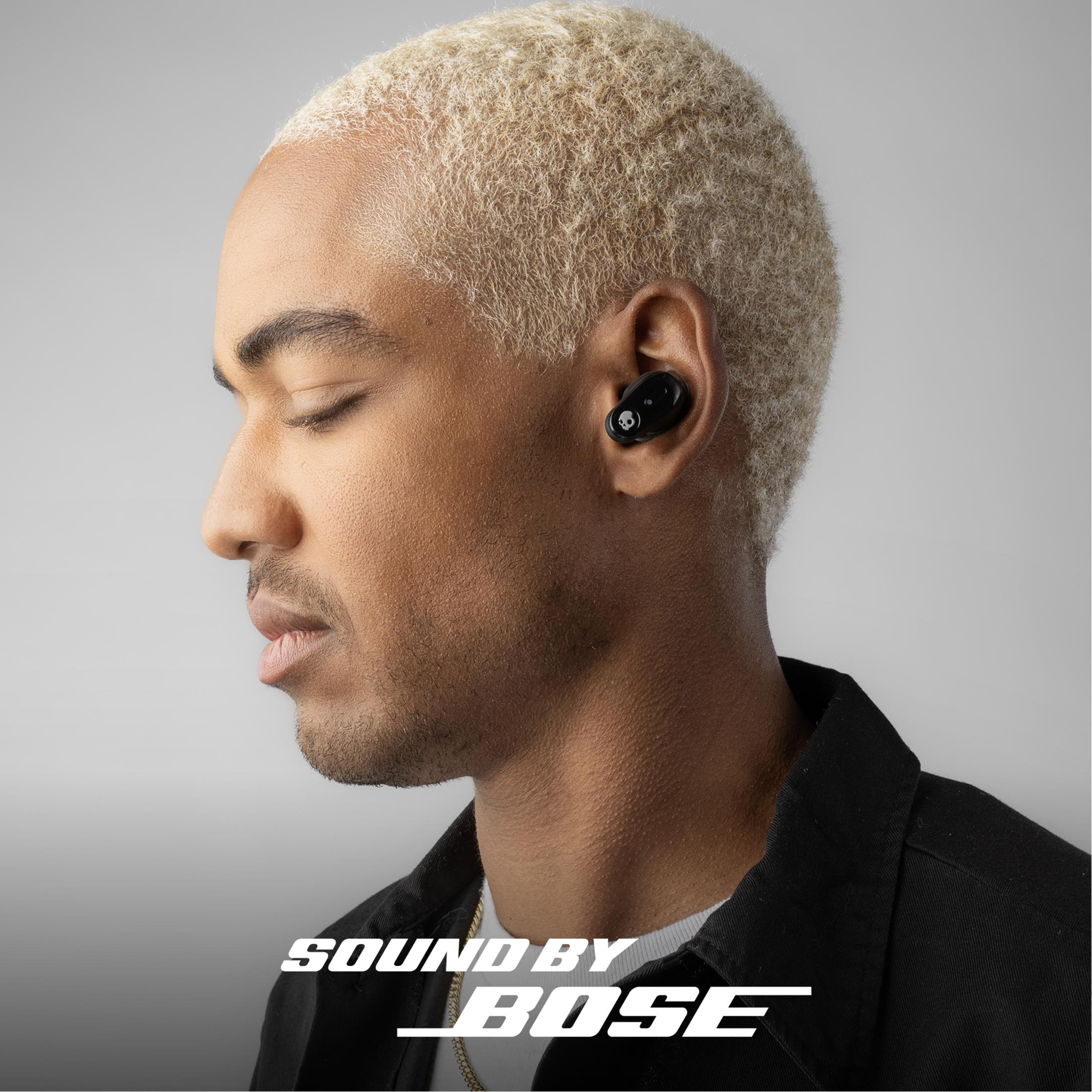 Hombre con pelo rubio lleva auriculares negros. Logo de Bose abajo.