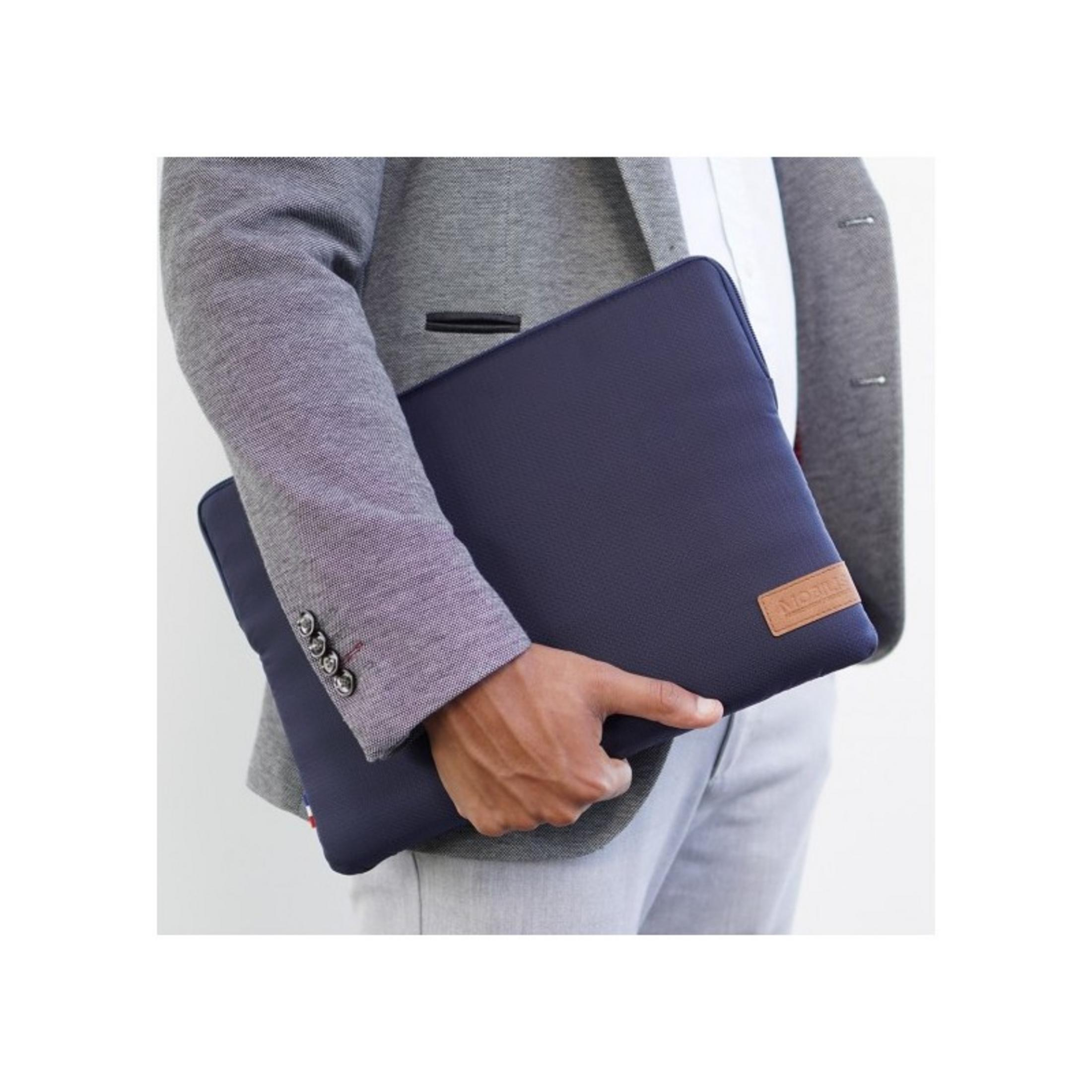 Uomo in blazer grigio tiene custodia blu navy per laptop con logo.