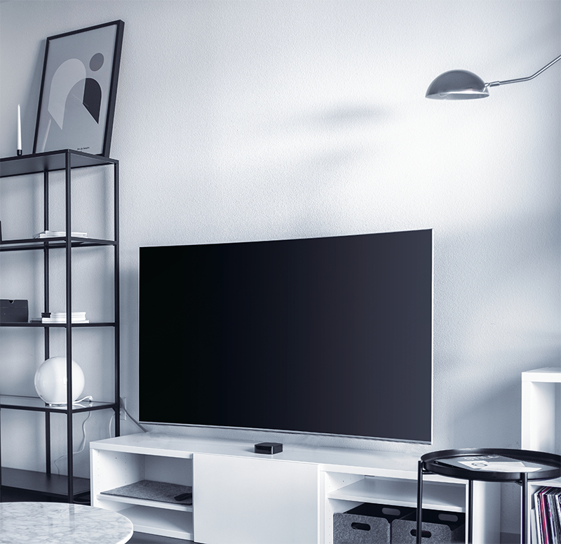 Ein großer schwarzer Fernseher steht auf einem weißen Schrank. Daneben ein Regal.