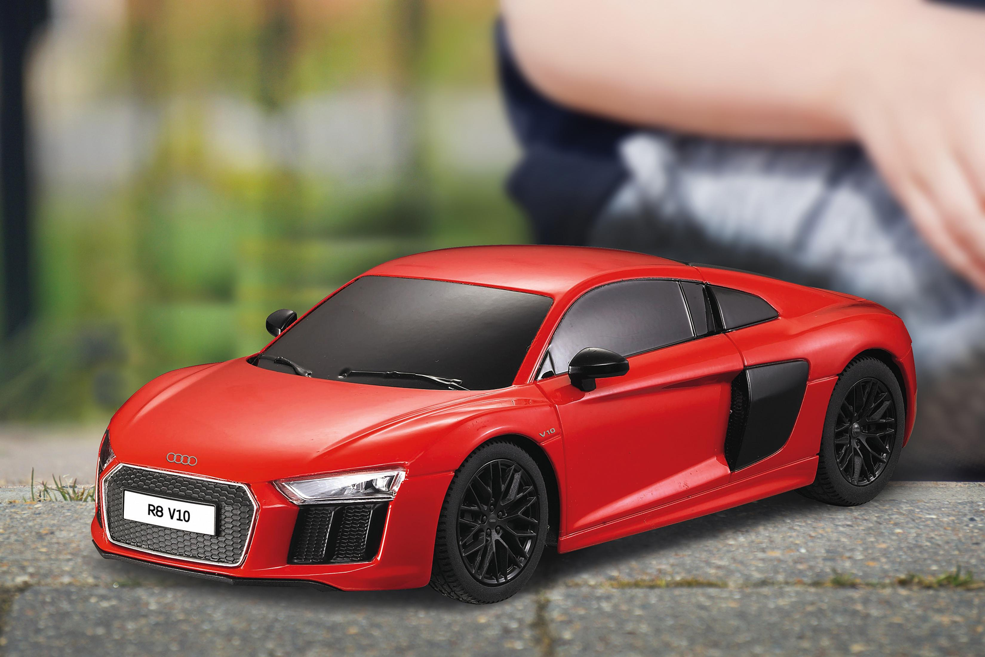 Un coche de juguete rojo Audi R8 V10 con ruedas negras está en una acera.
