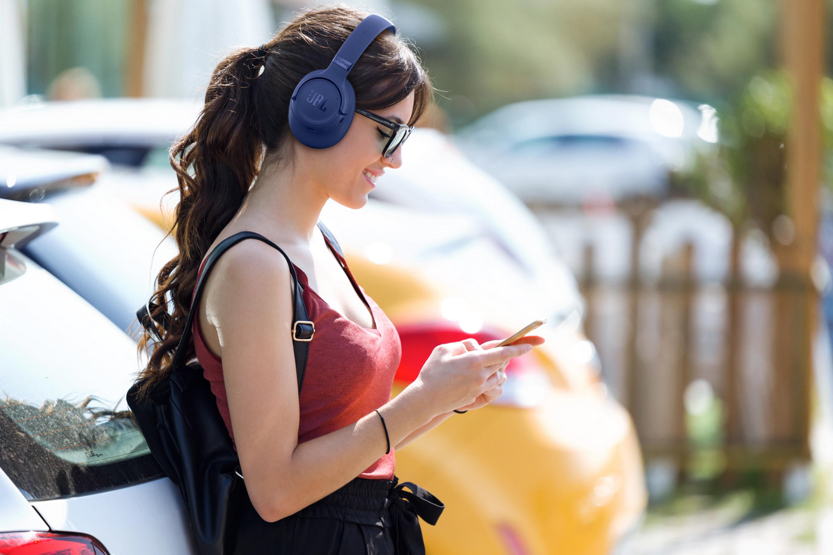 Una donna con cuffie e occhiali usa il suo smartphone all'aperto vicino alle auto.