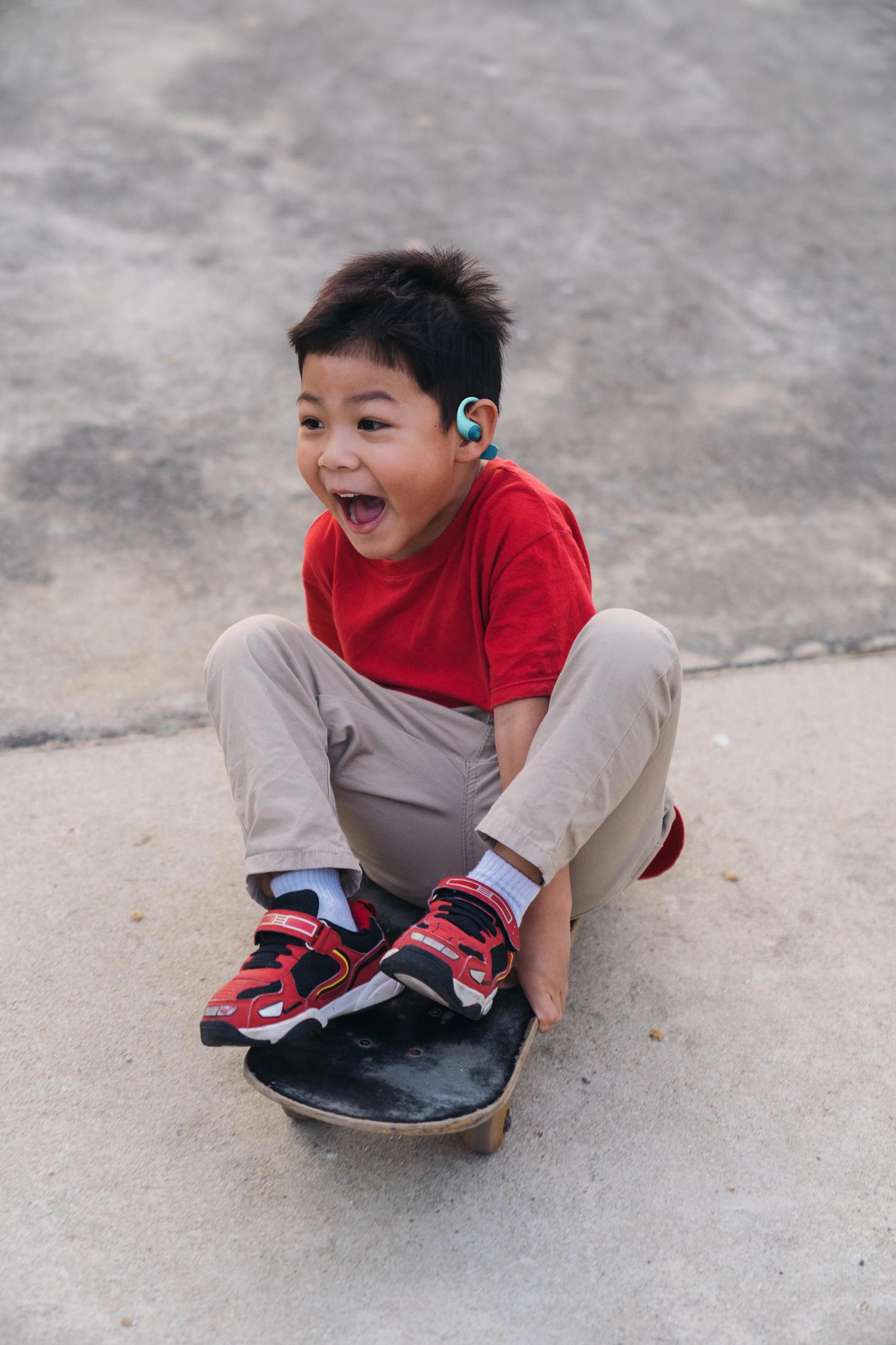 Un niño con camisa roja y pantalones caqui se sienta en un monopatín.