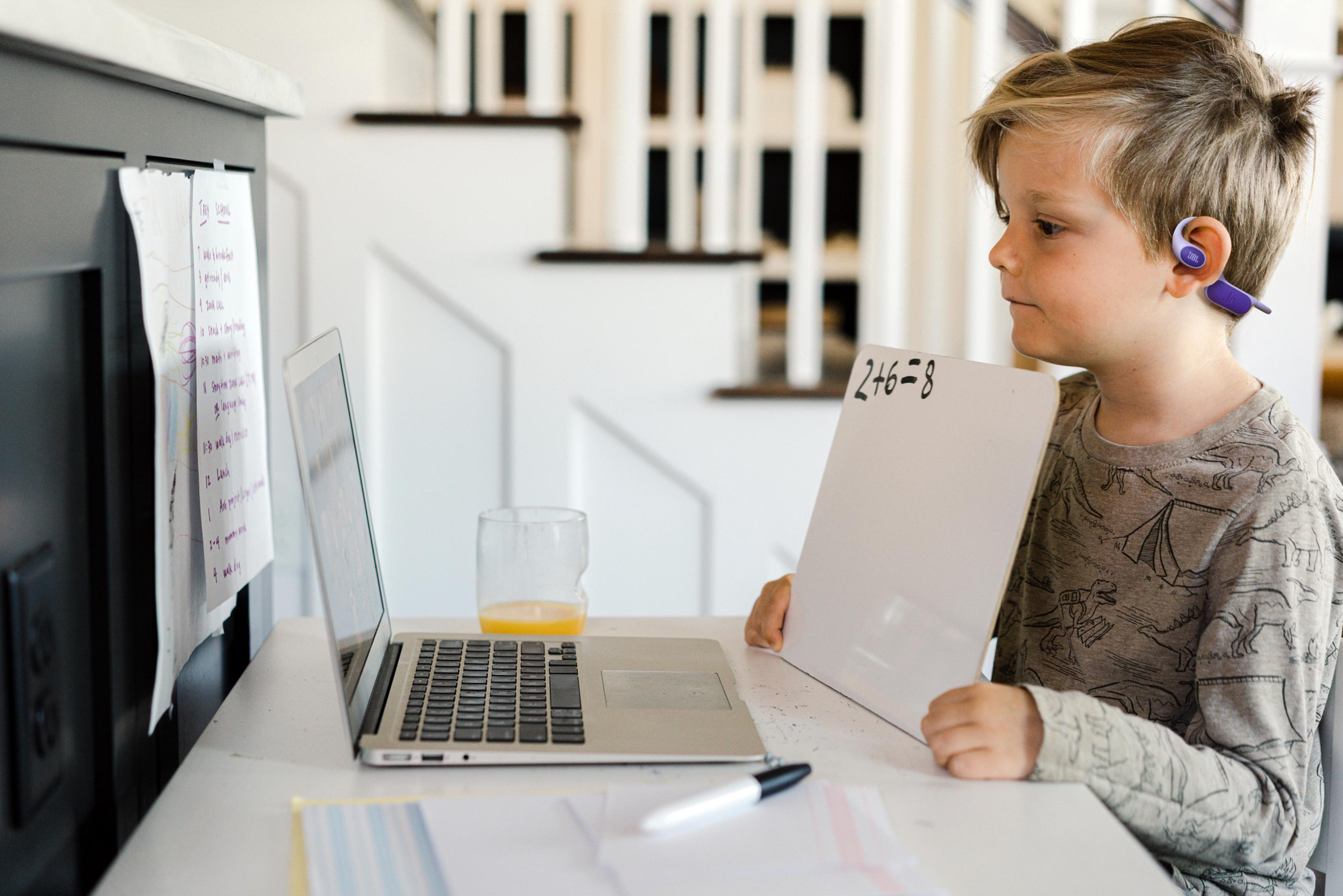 Un niño con auriculares aprende en línea usando una laptop y una pizarra.
