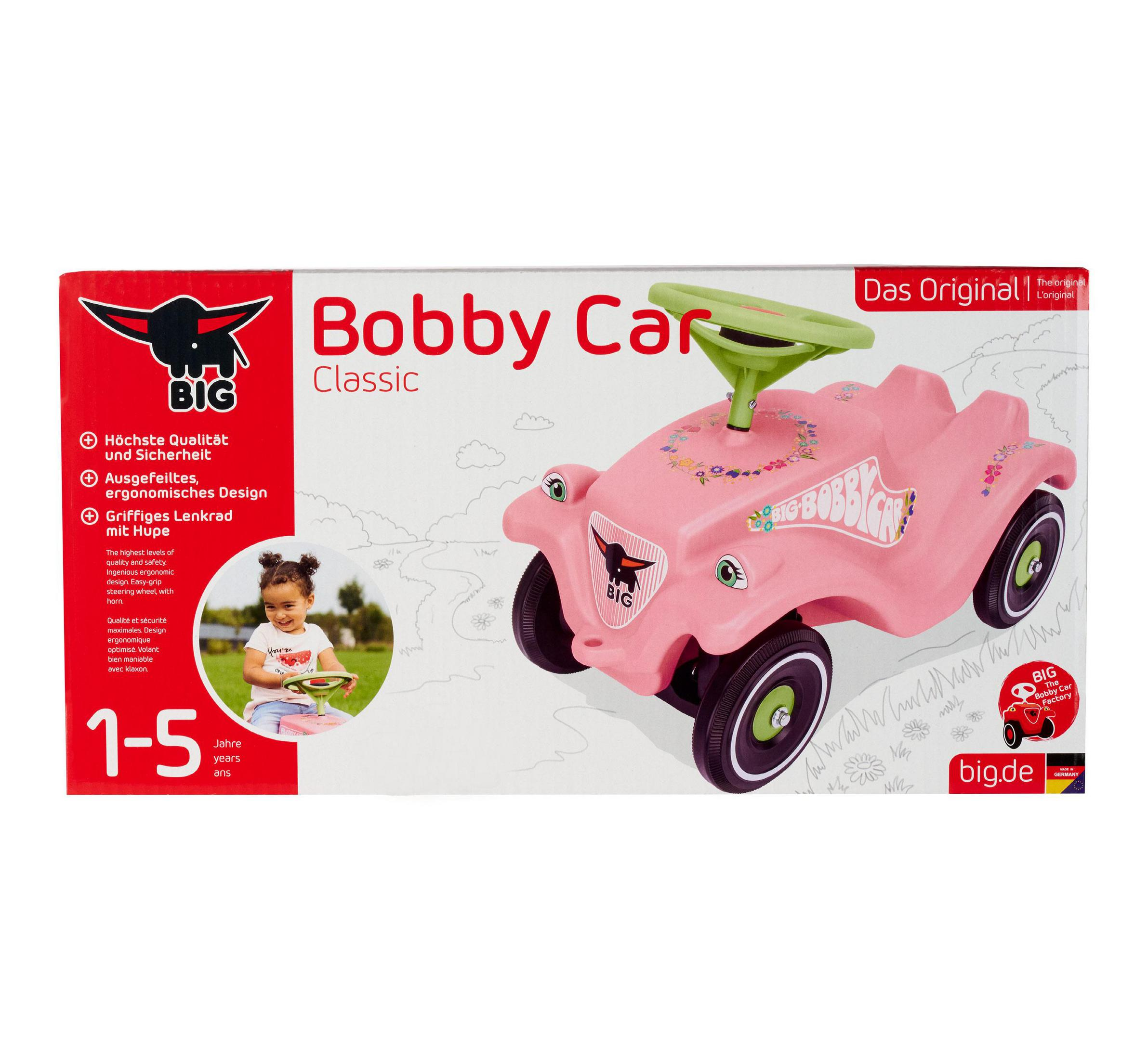 Ein rosa Bobby Car Classic mit grünem Lenkrad und Aufklebern. Ein Kind sitzt darauf.