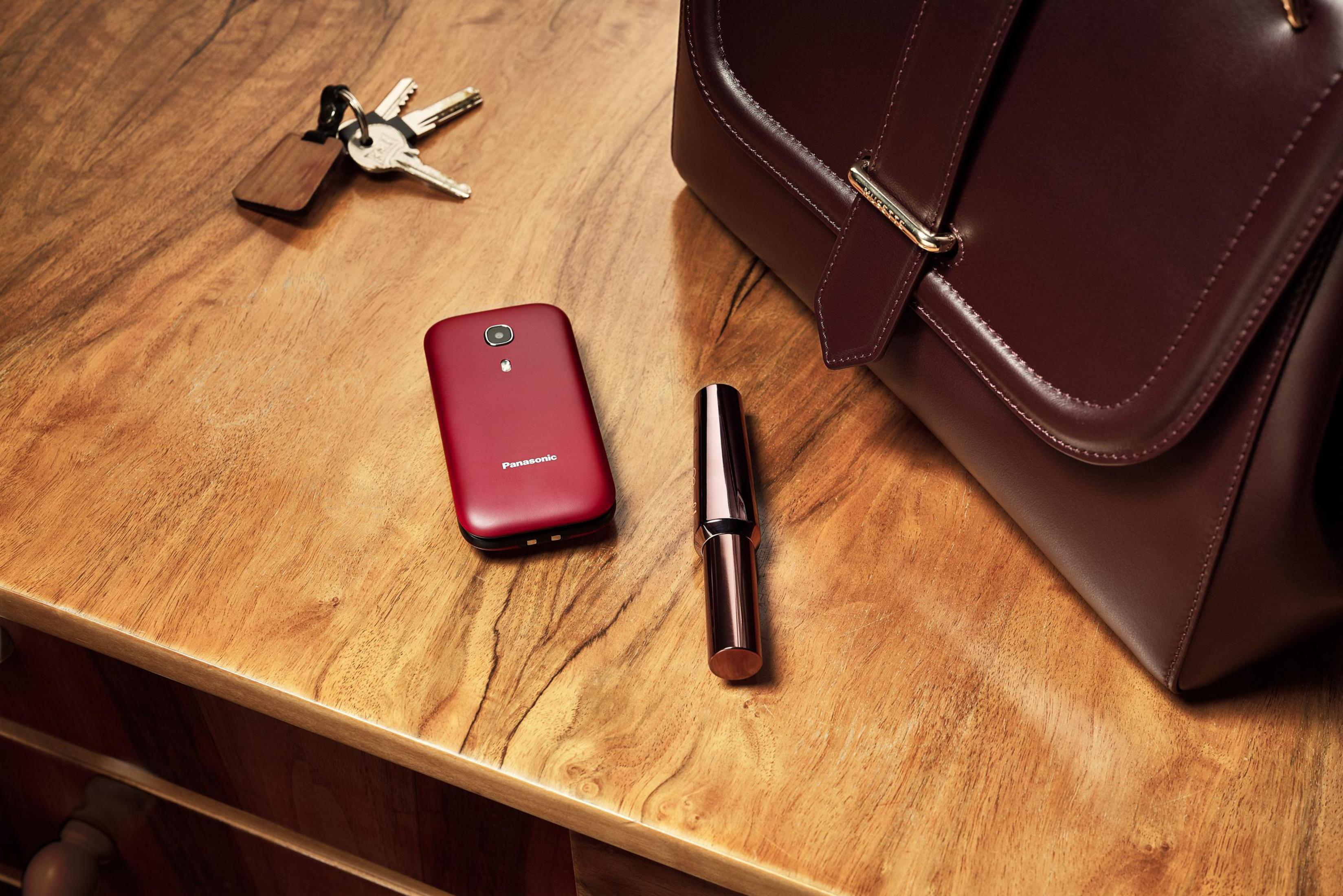 Telefono rosso, mazzo di chiavi, rossetto e borsa in pelle marrone su legno.