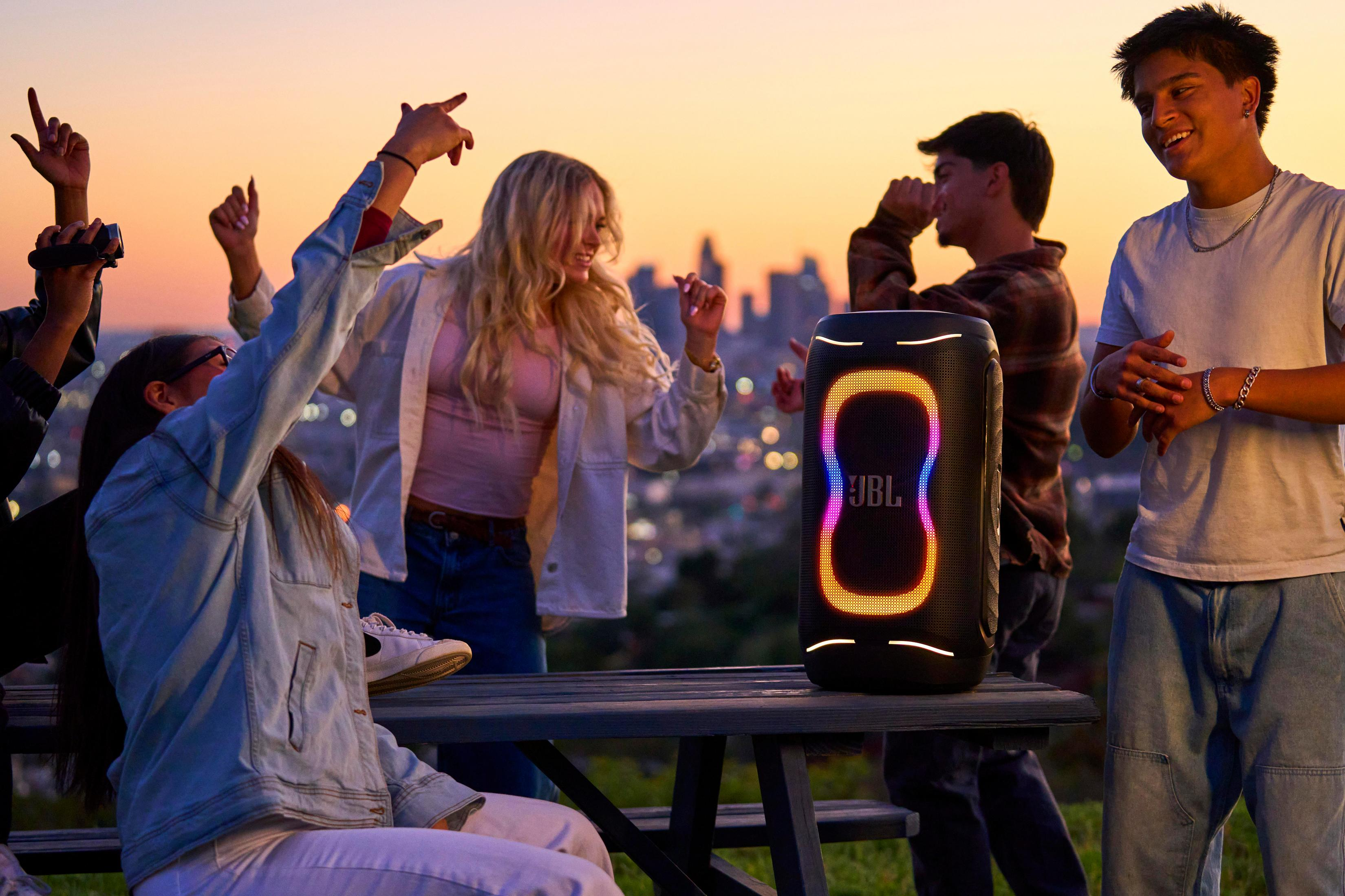 Gente joven bailando al atardecer con un altavoz JBL.