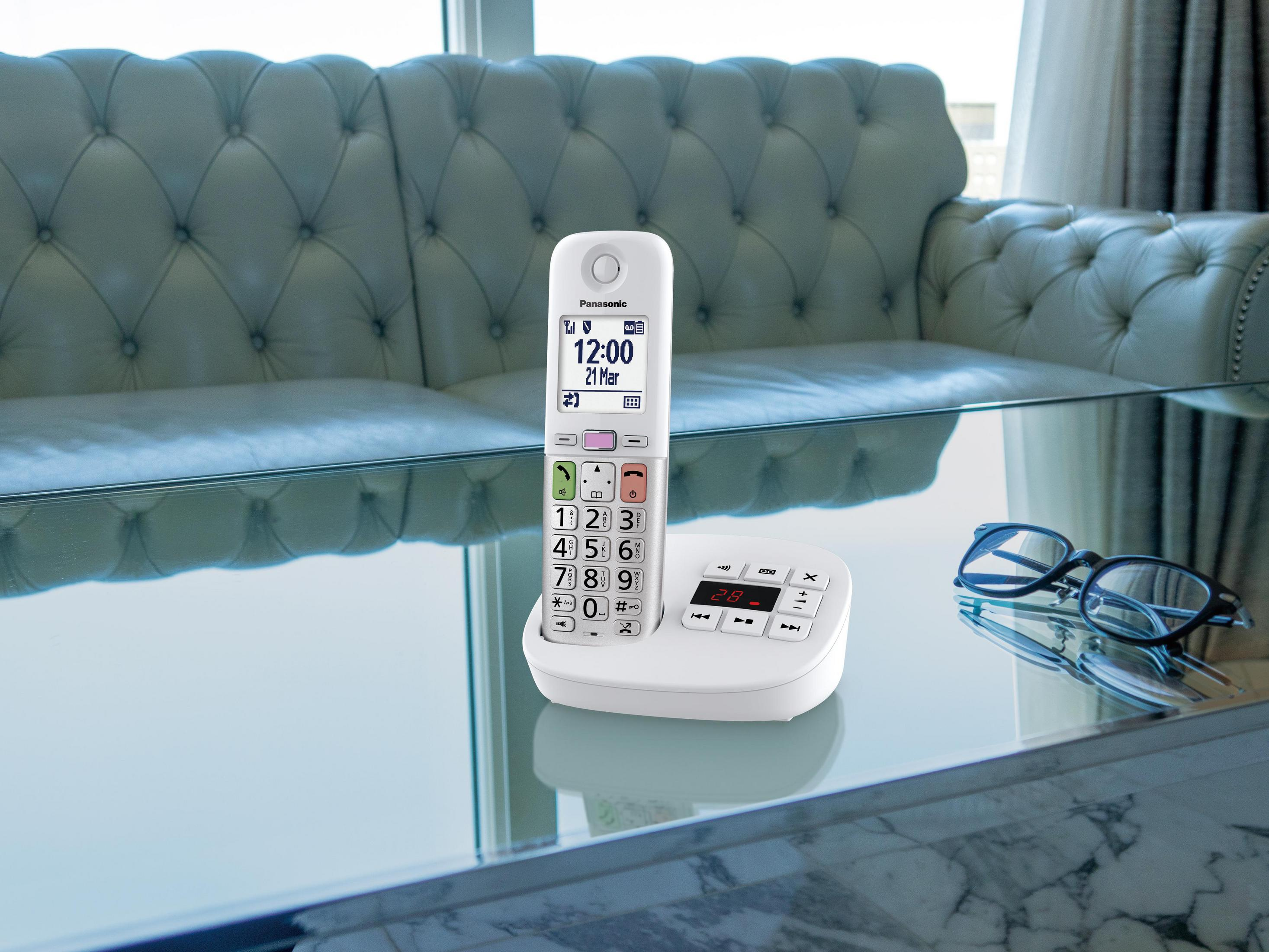 Un telefono cordless bianco è su un tavolino di vetro accanto a un paio di occhiali.