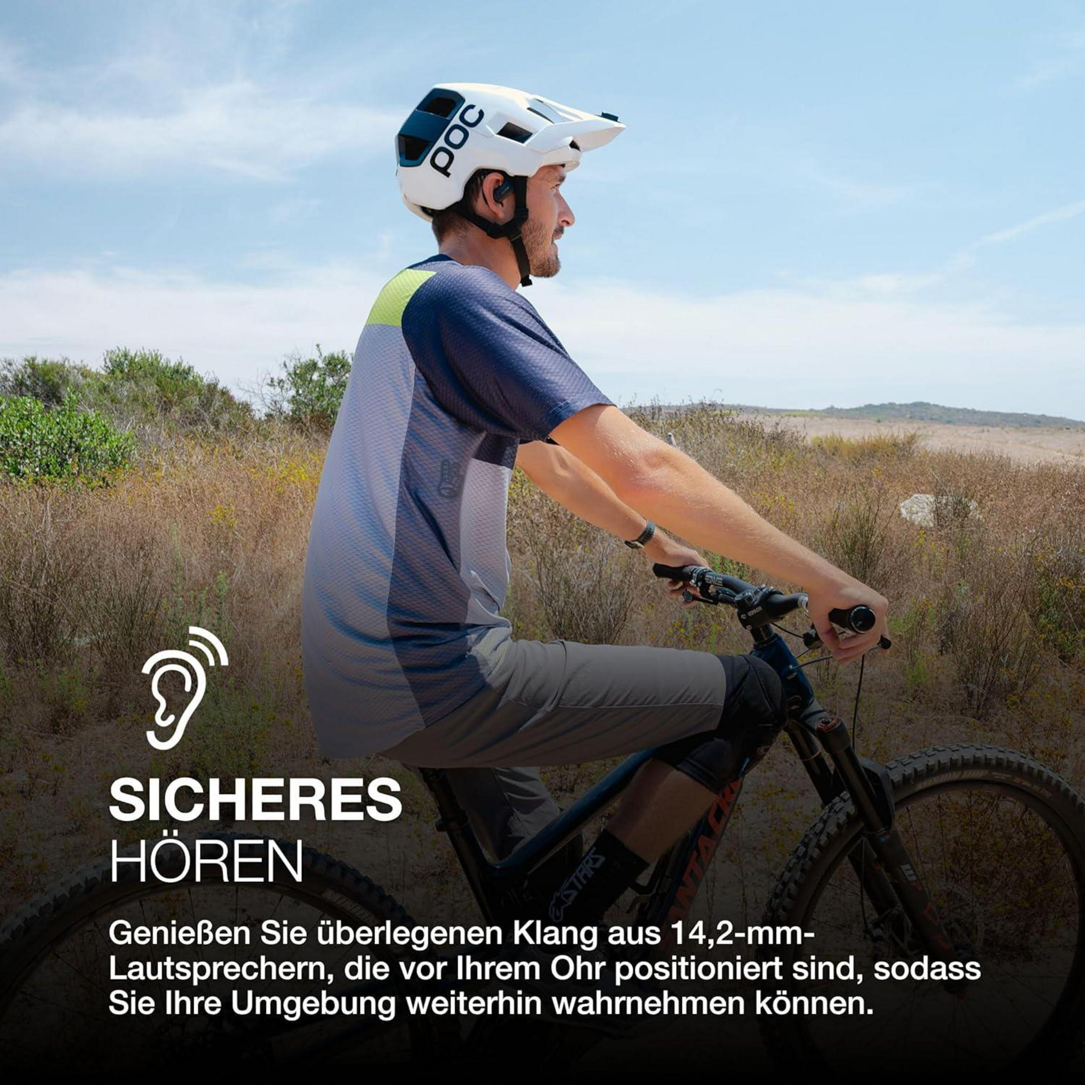 Un uomo va in mountain bike con casco e auricolari in un paesaggio roccioso.