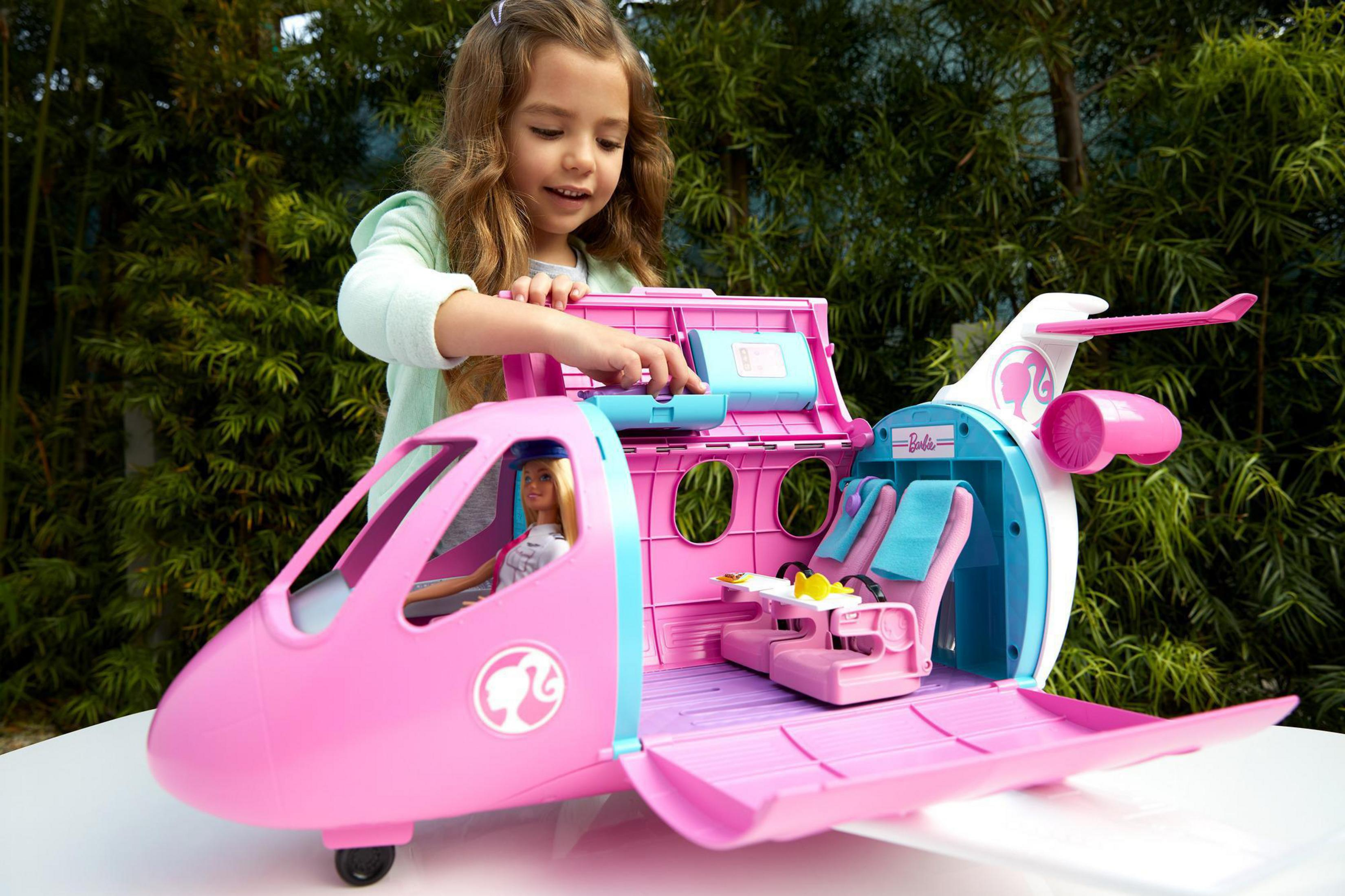 Ein Mädchen spielt mit einem rosa Barbie-Flugzeugspielzeug im Freien.