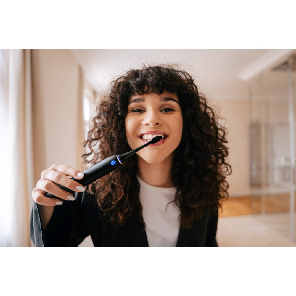 Una donna con i capelli ricci si lava i denti con uno spazzolino elettrico nero.