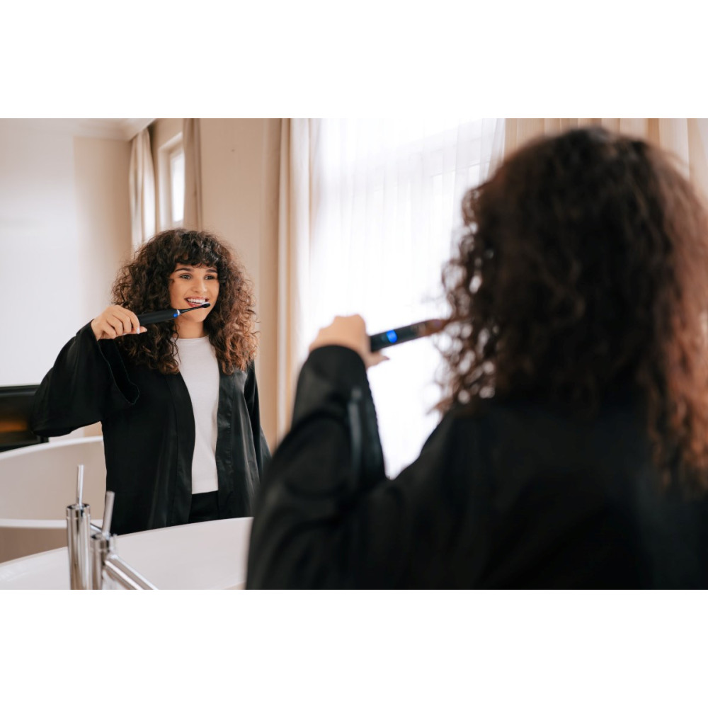 Donna con capelli ricci si lava i denti con spazzolino elettrico davanti allo specchio.