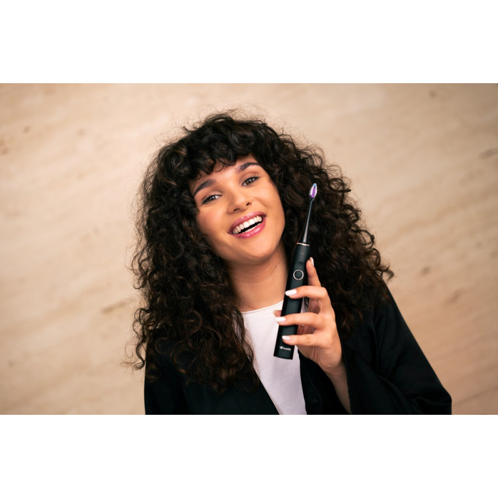 Una donna con capelli ricci tiene uno spazzolino elettrico nero con setole viola.