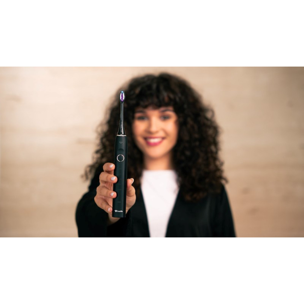 Una donna con i capelli ricci tiene uno spazzolino elettrico nero con setole viola.