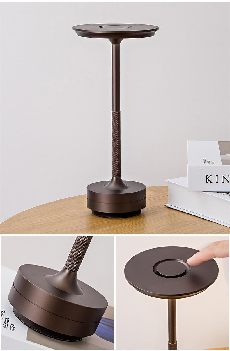 Eine dunkle Metall-Tischlampe mit rundem Sockel und Schalter steht auf einem Holztisch.